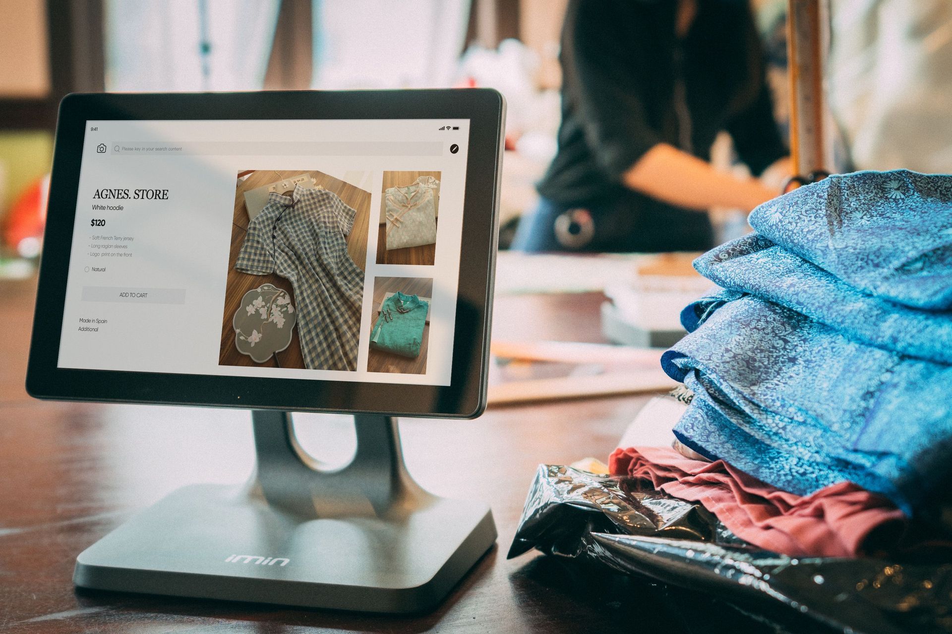 Tablet showing a clothing website beside folded blue and pink garments in a shop