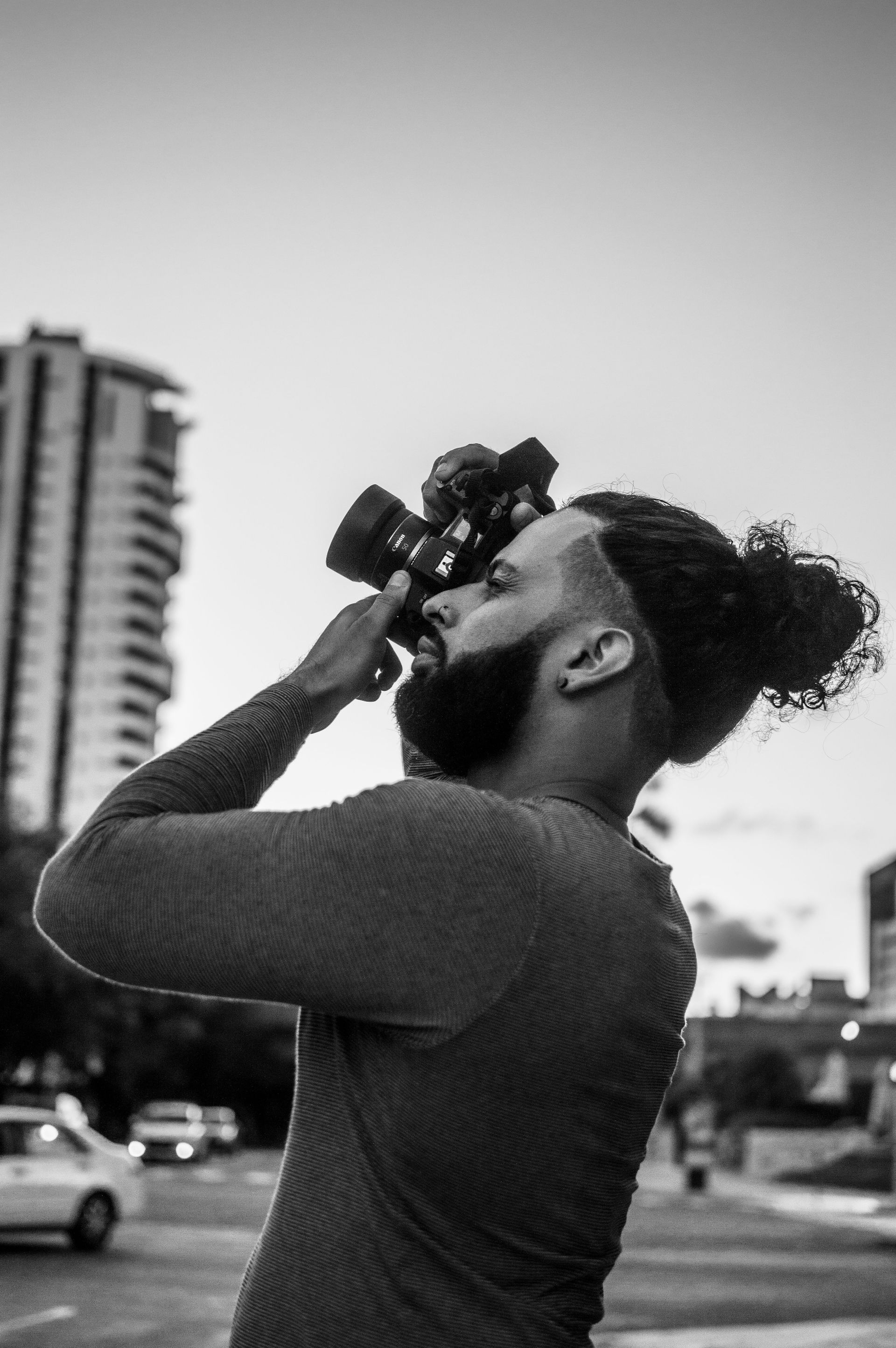 Person looking through binoculars on a city street, with buildings in the background