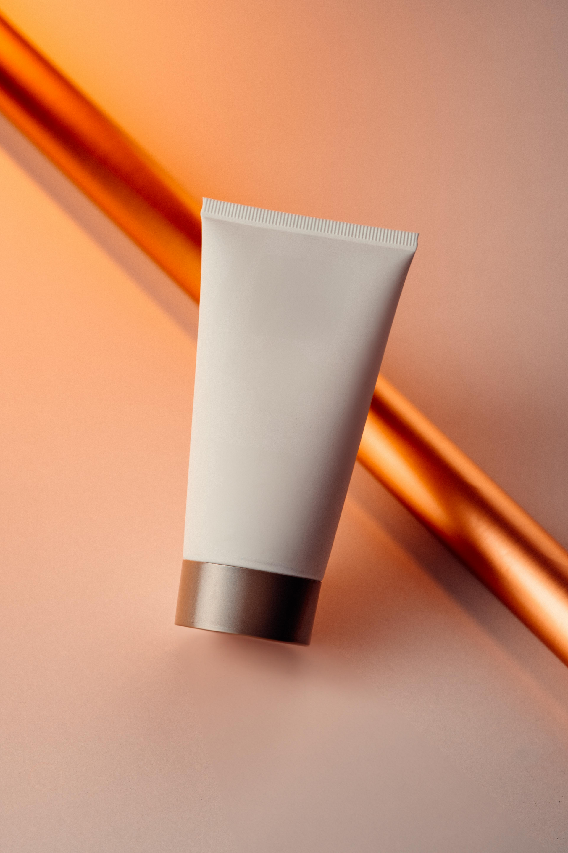 White cosmetic tube with silver cap on a peach background with diagonal orange stripes