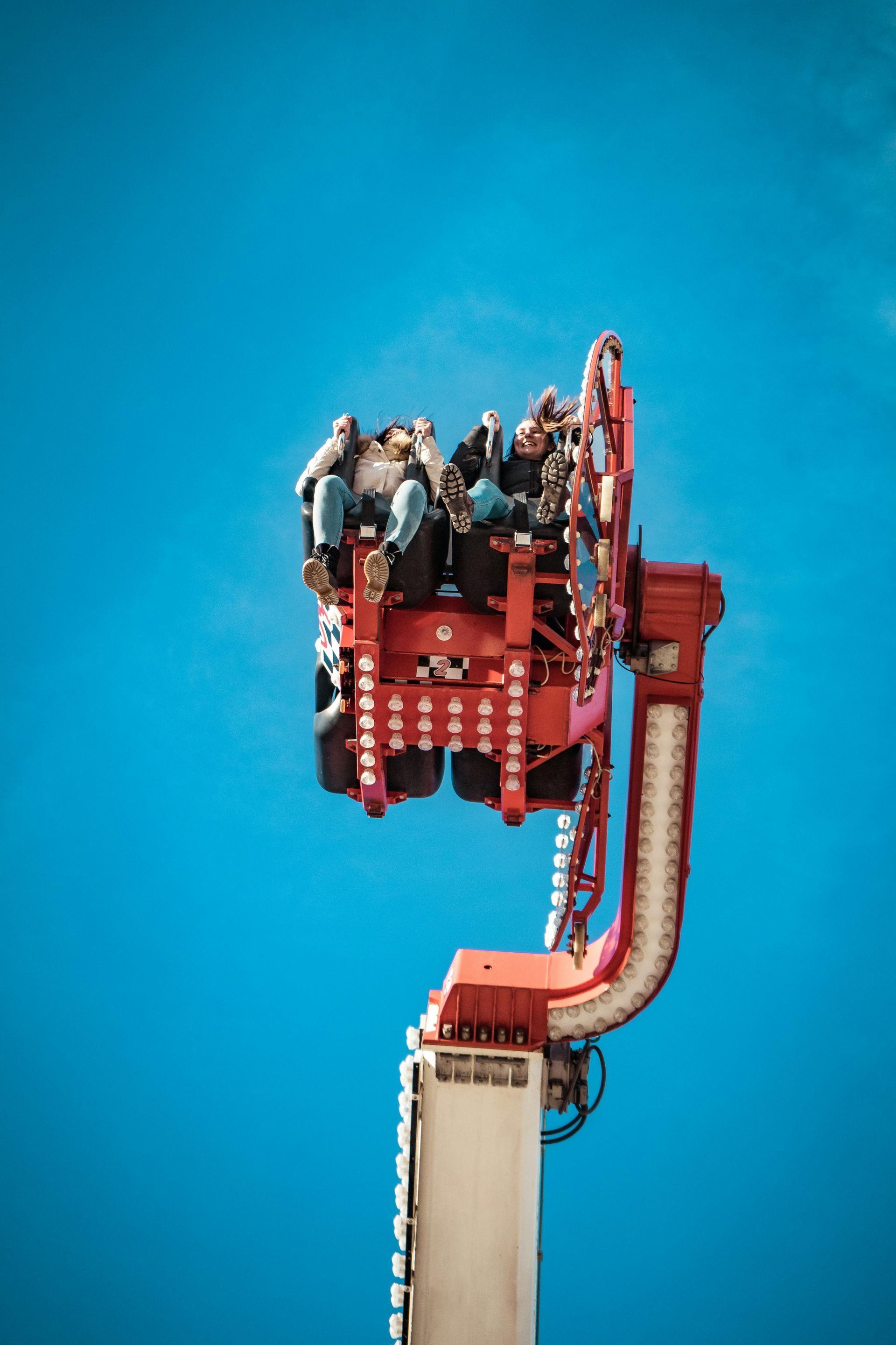 Red and white amusement park ride with people against a bright blue sky.