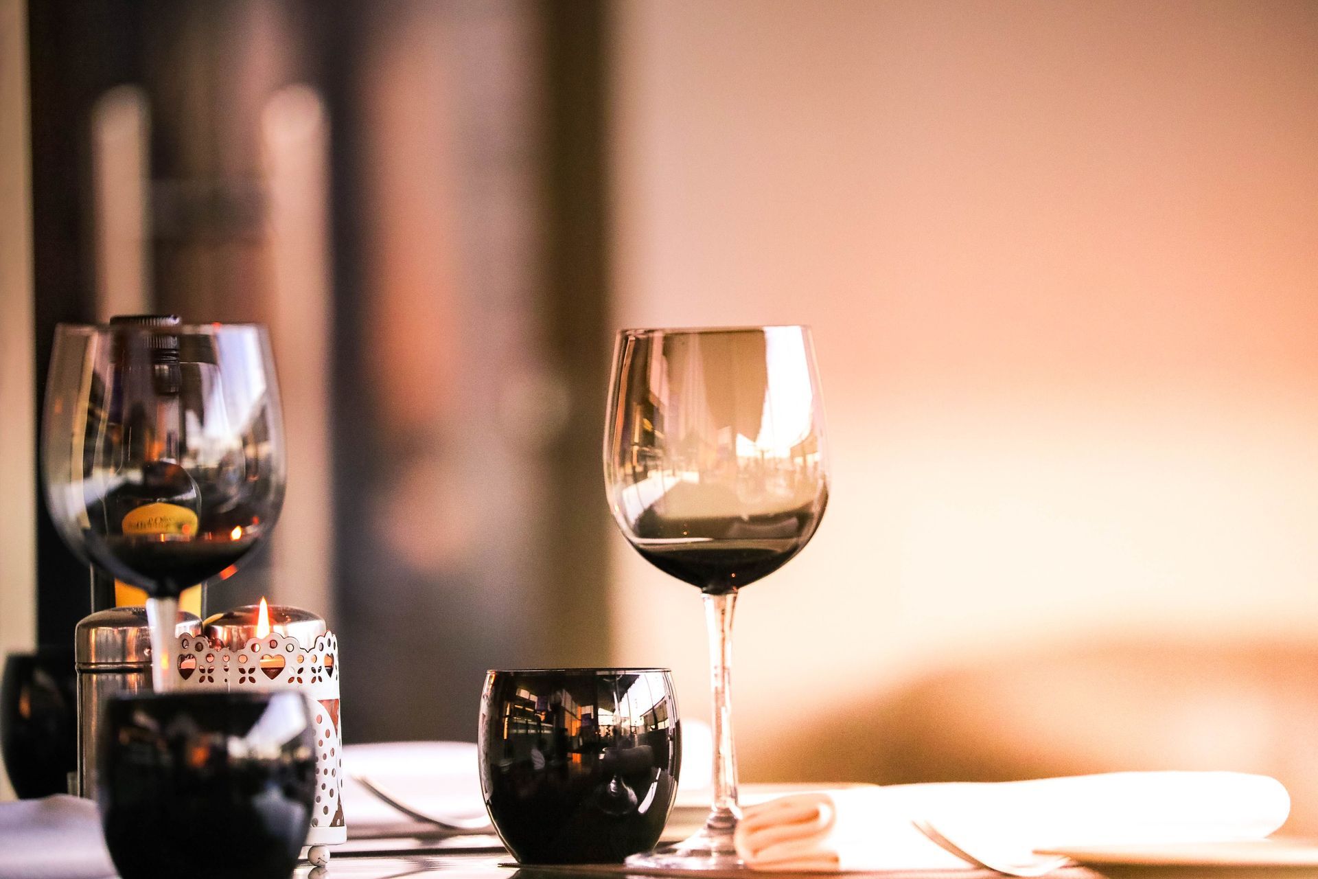 Two wine glasses and dark candles on a table in a softly lit restaurant setting