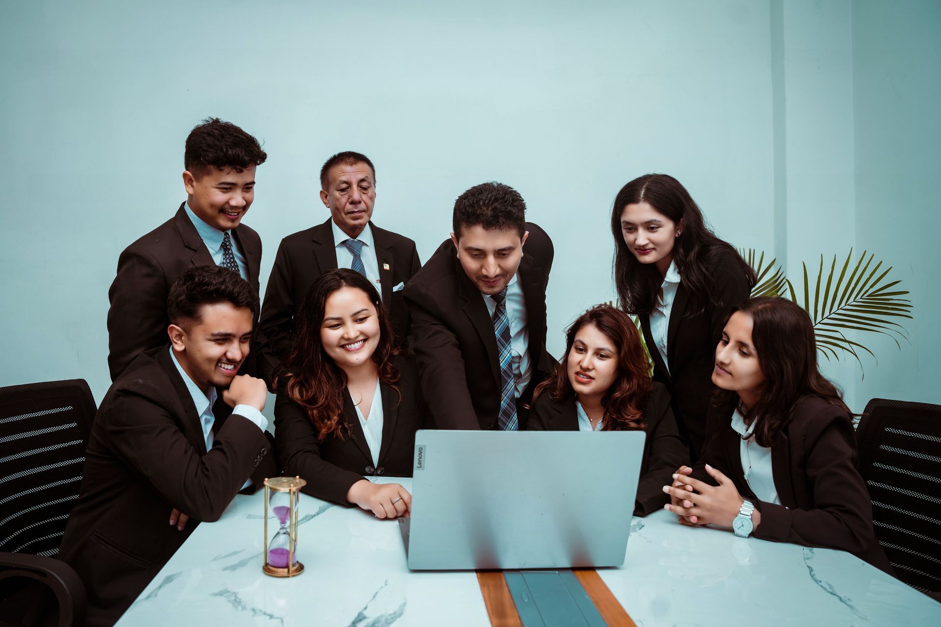 Team of professionals gathered around a laptop in a meeting room, smiling and discussing together.