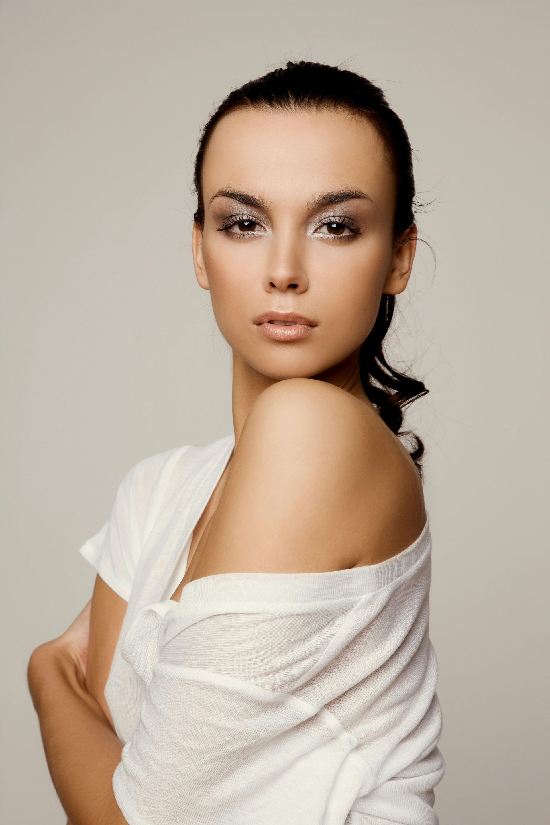 Woman with dark hair in a white shirt, looking at the camera. Soft lighting, neutral background.