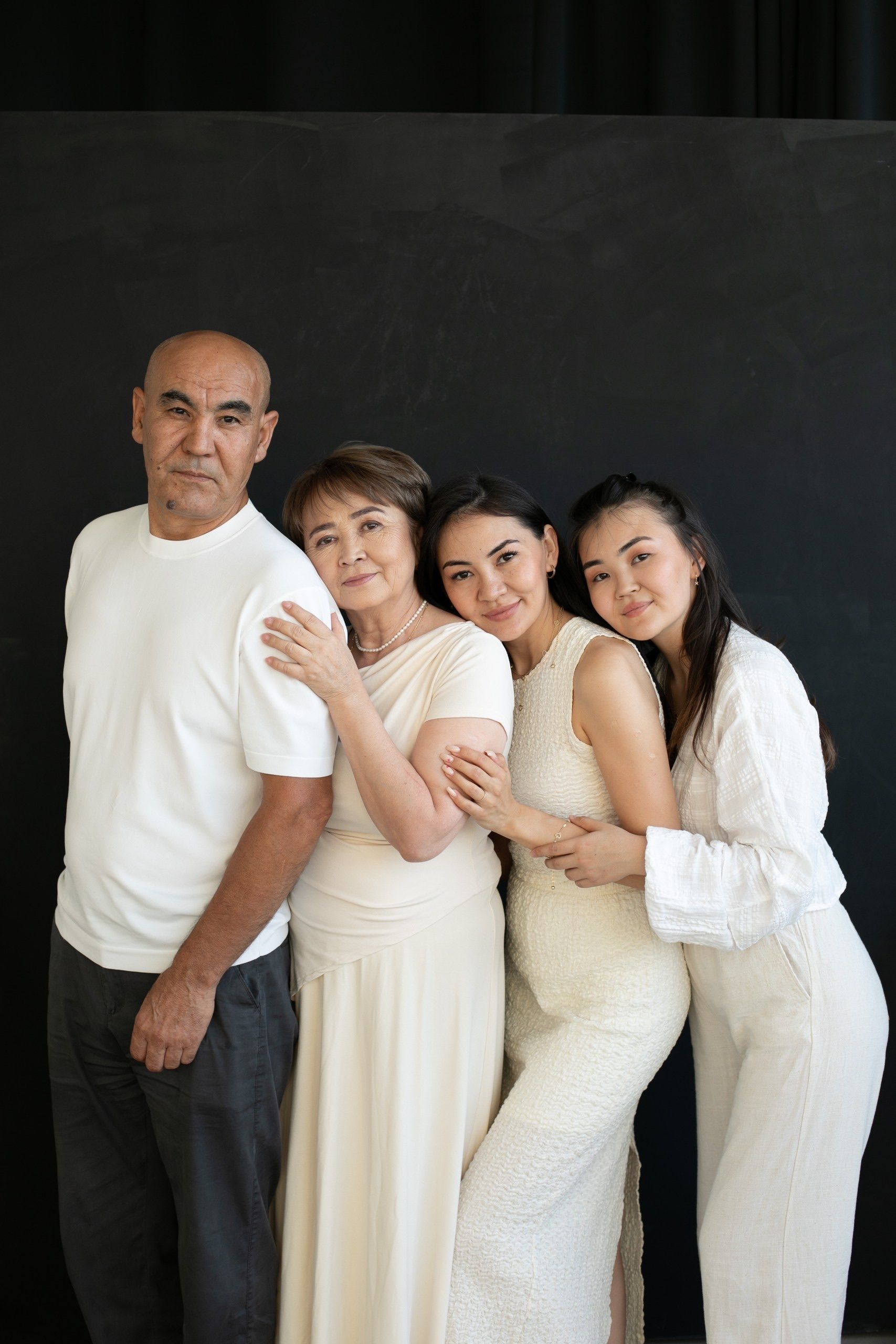Four people in white outfits posing closely against a dark backdrop.