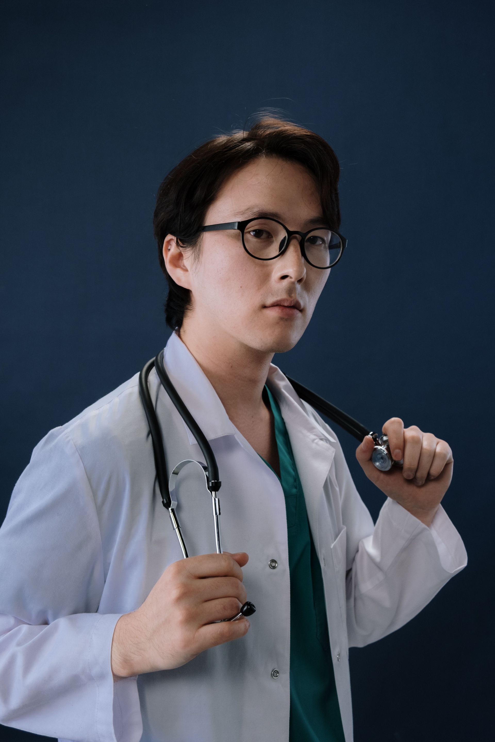 Doctor in a white coat holding a stethoscope against a dark blue background.