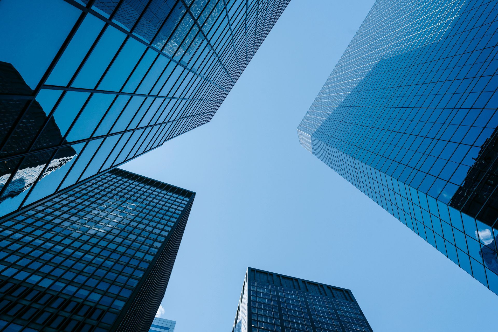 Looking up at blue glass skyscrapers converging around a bright sky