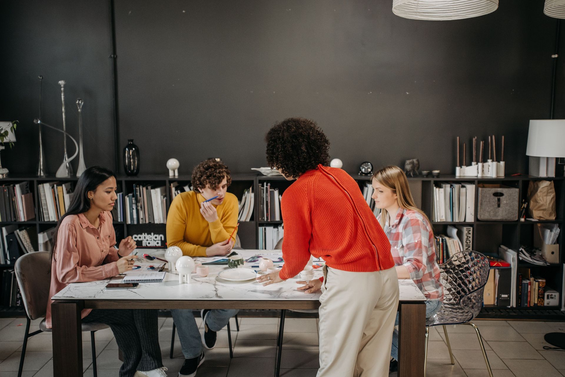 People gathered around a table in a studio, collaborating on papers and art supplies.