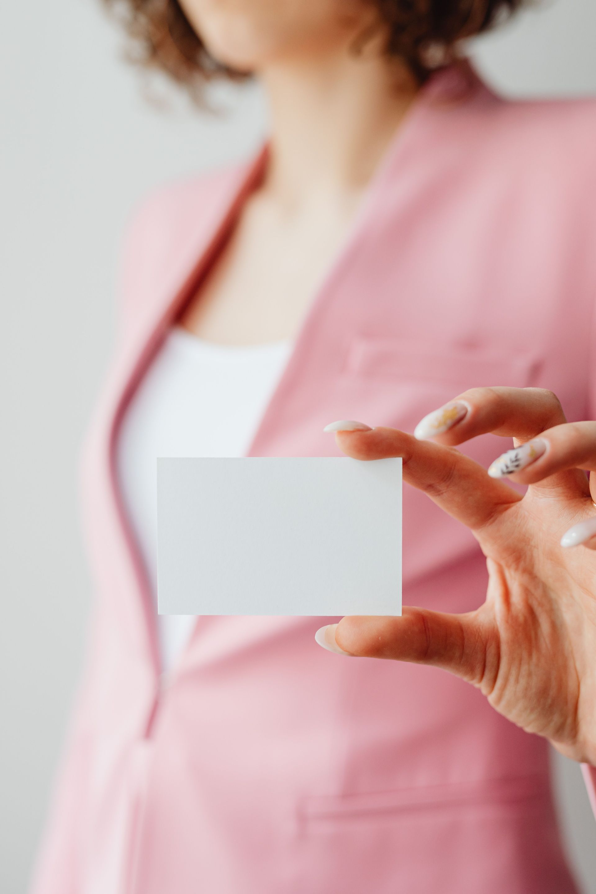 Person in pink blazer holding a blank white card in front of their torso.