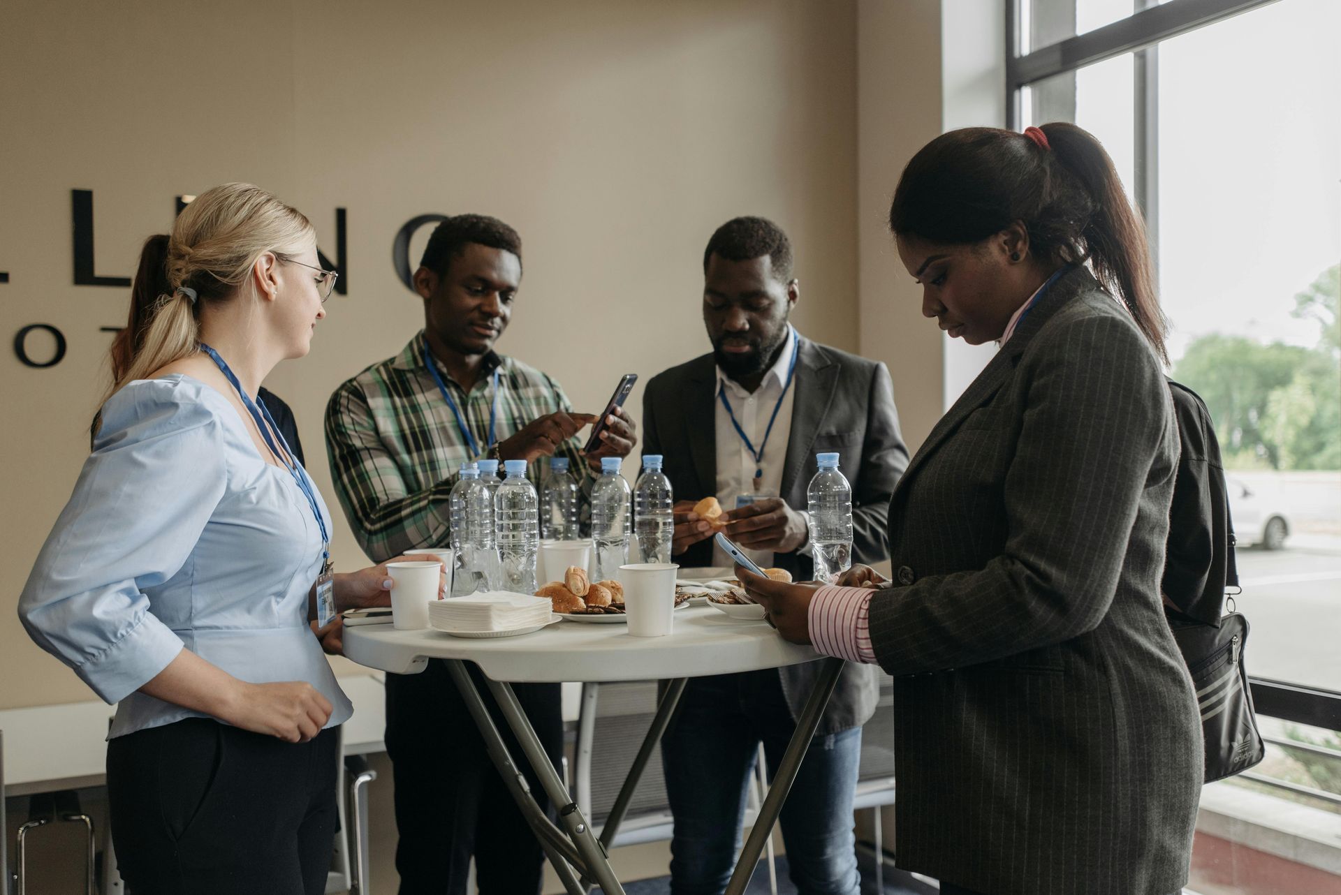 People at a networking event around a table. Some are on phones, while others converse.