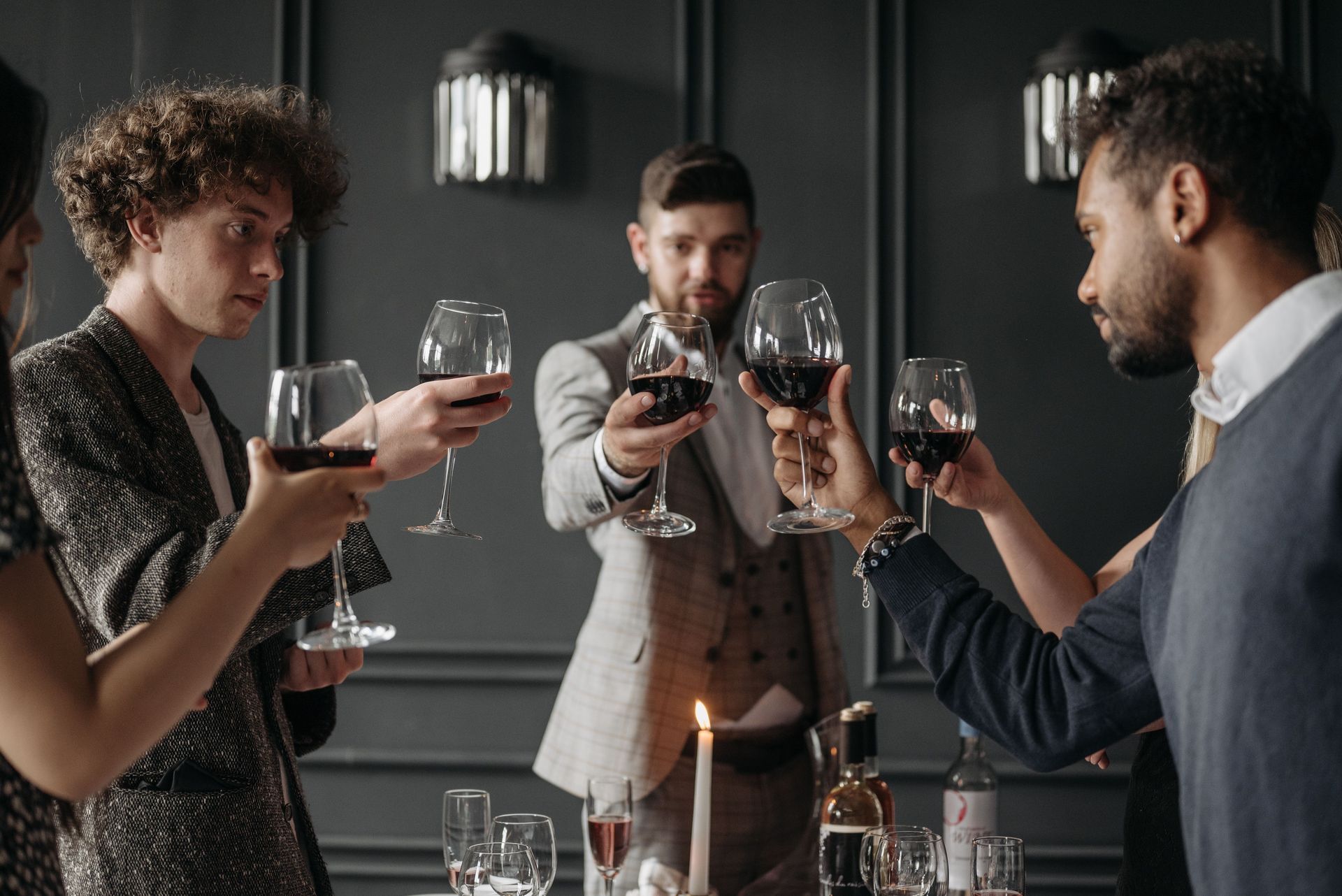 Friends toasting wine glasses around a candlelit dining table in a dark, modern room