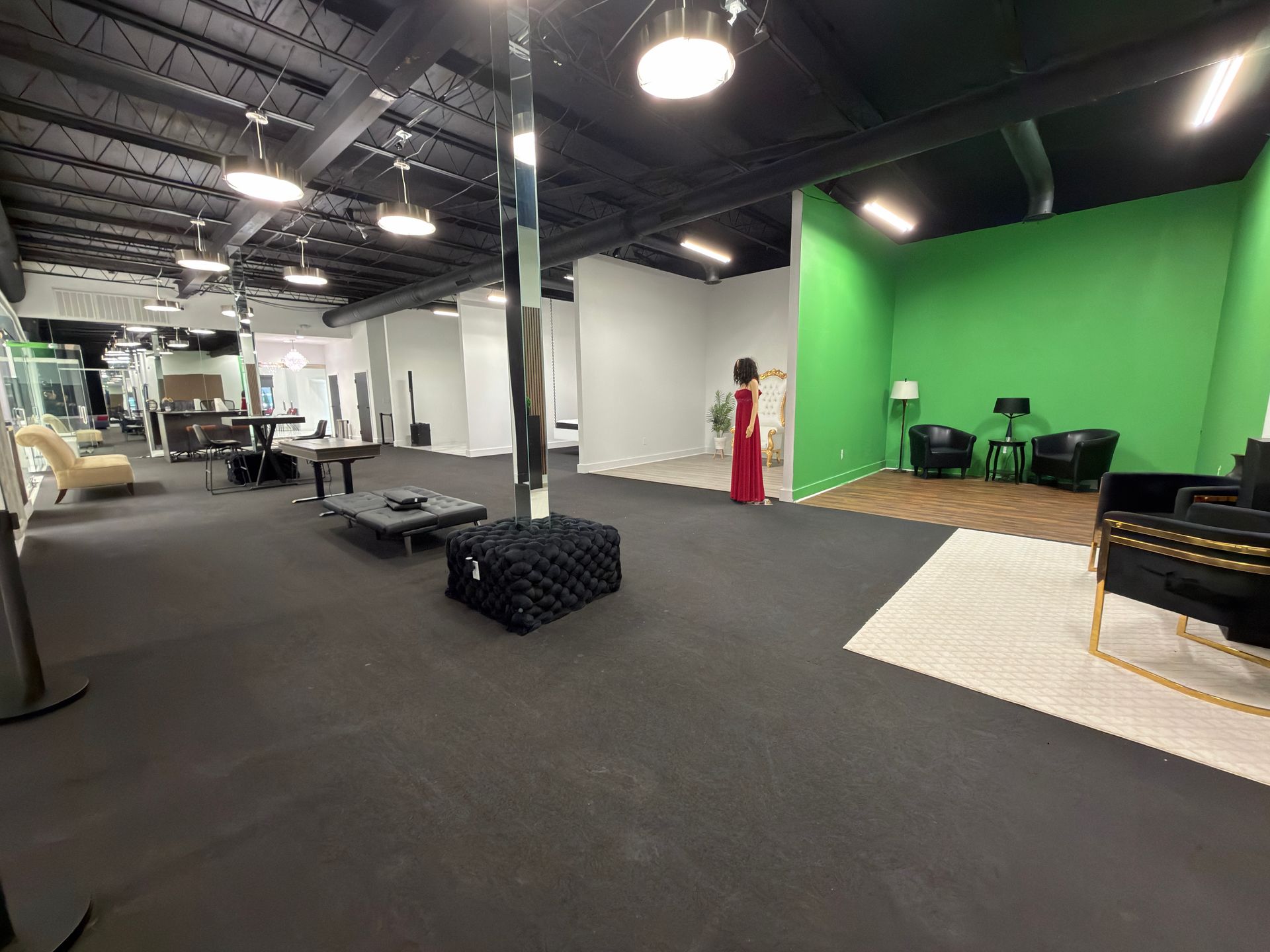 Empty studio with green screen wall, staging platforms, and overhead lights in a large open room
