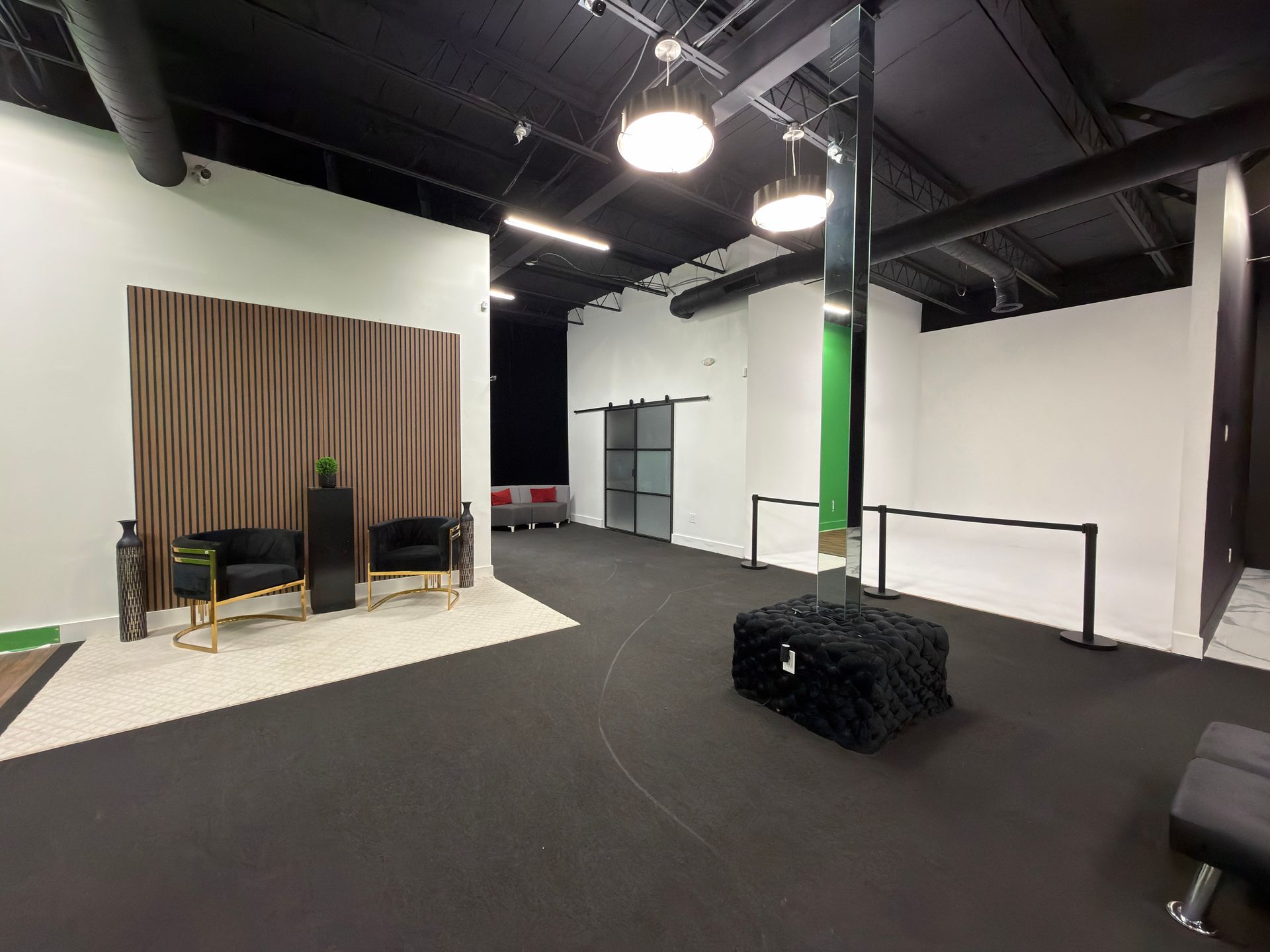 Empty studio with black carpet, white walls, curtain backdrop, chairs, and hanging lights