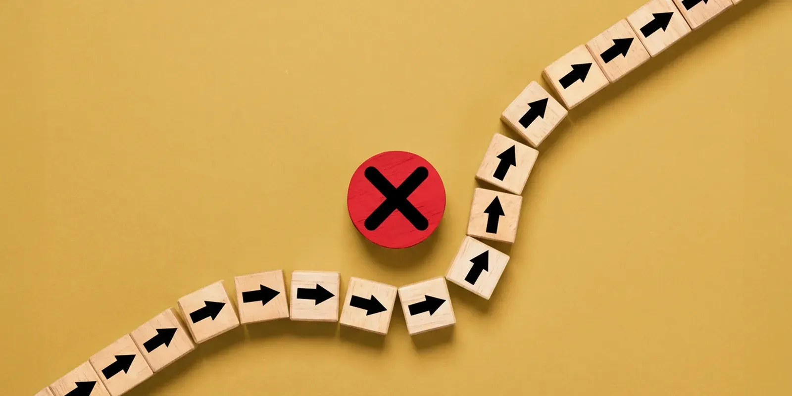 A line of wooden blocks with black arrows curves around a large, red circular sign featuring a black 