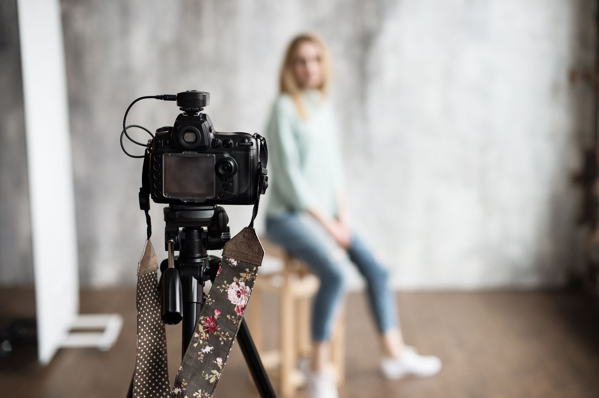 A woman is sitting on a stool in front of a camera on a tripod.