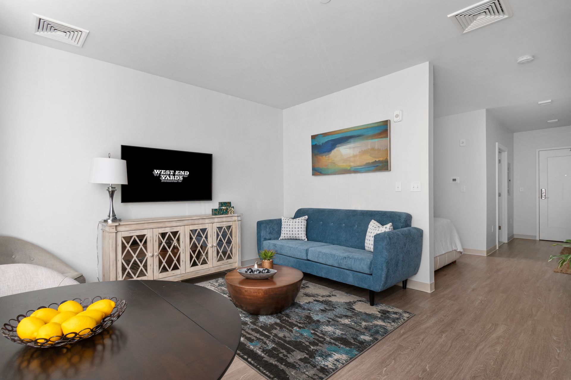 Apartment living room with sofa, rug, wall art, TV, and TV stand at West End Yards.