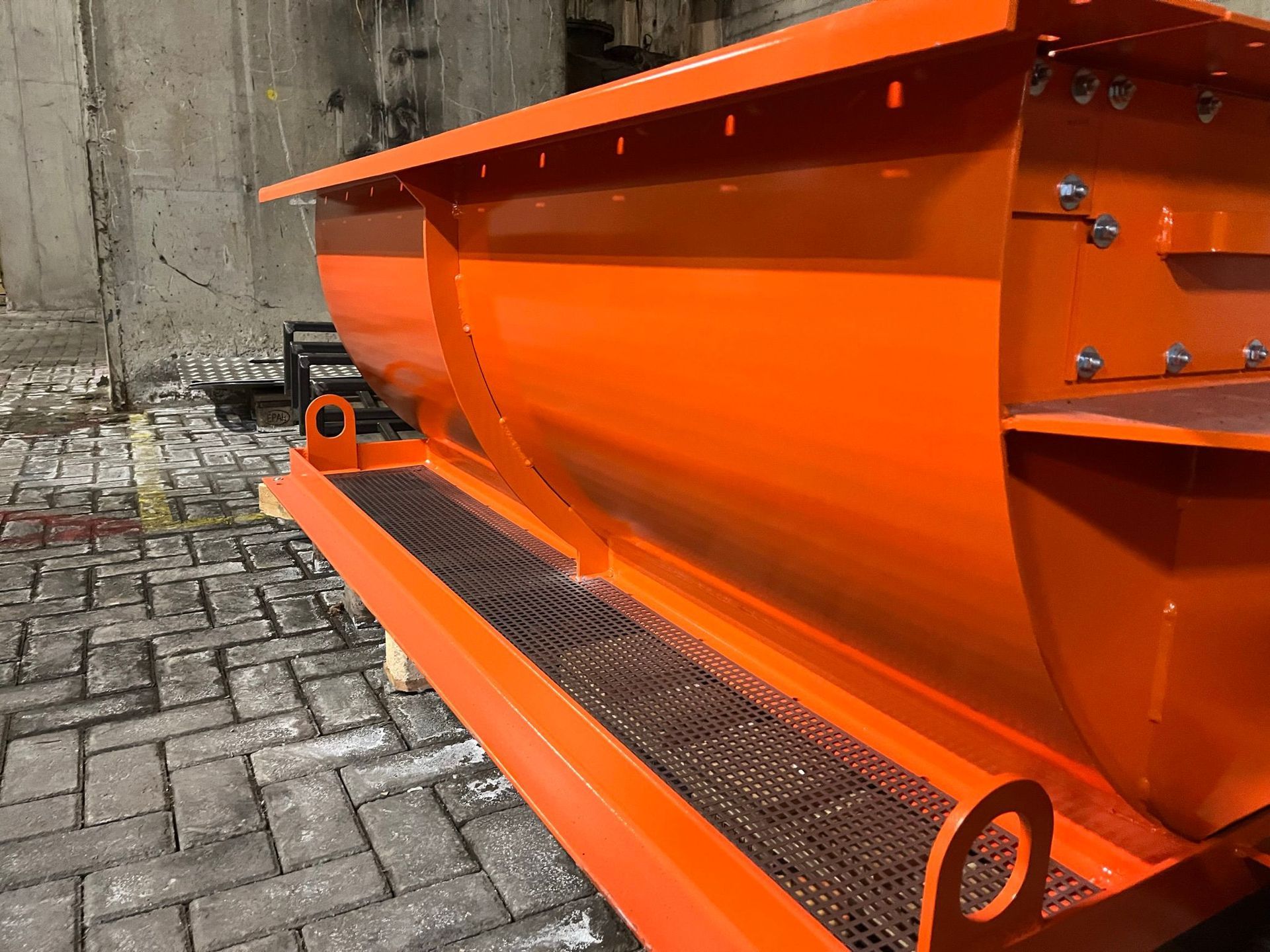 Feloranje metalen trog met gaasbodem, bouten en bevestigingsogen, geplaatst op een baksteen.
