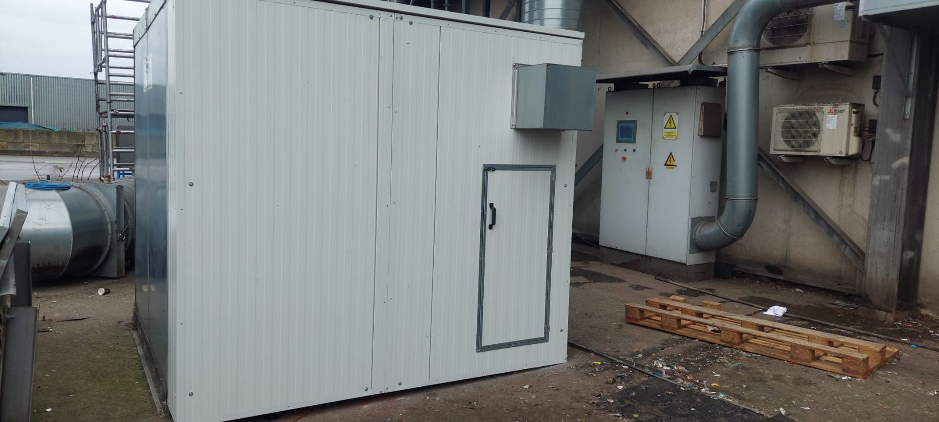 Wit industrieel gebouw met een deur en airconditioningunits aan de zijkant.