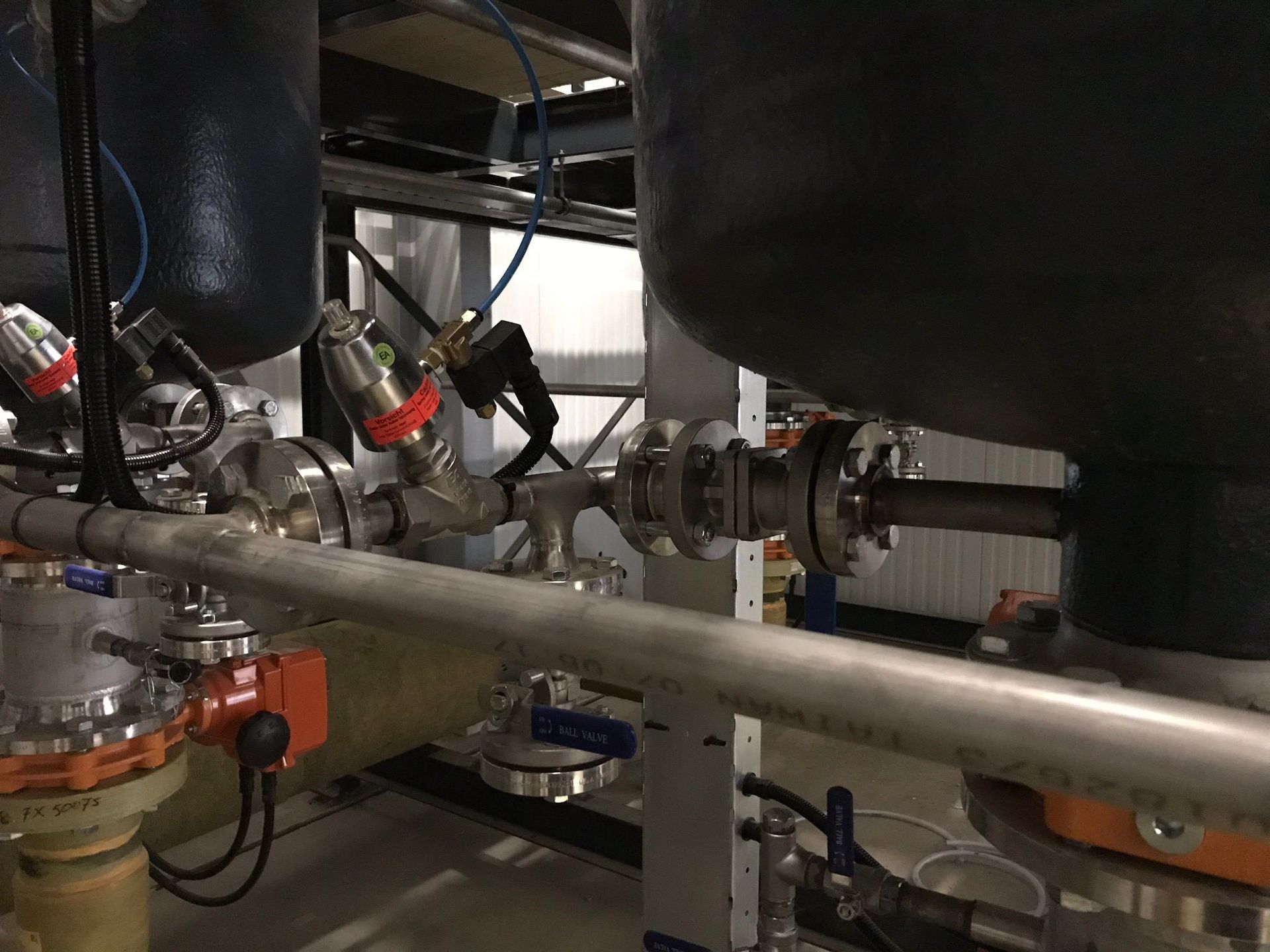 Industriële machines met leidingen, kleppen en geïsoleerde tanks in een fabriek.