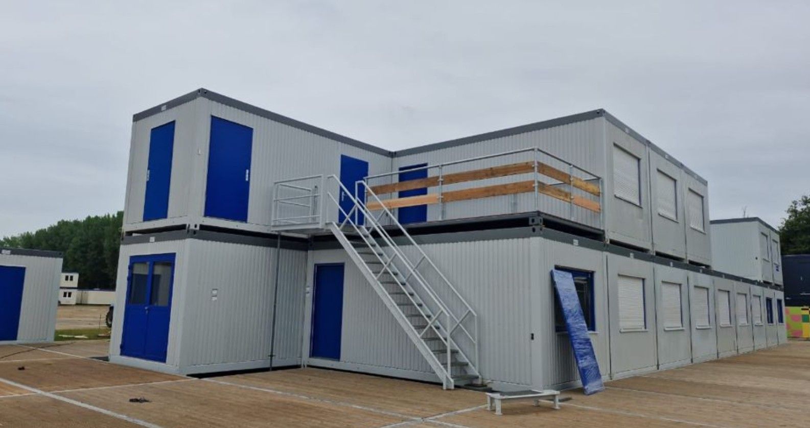 Modulaire gebouwen van twee verdiepingen met blauwe deuren en ramen, een metalen trap en een houten leuning.