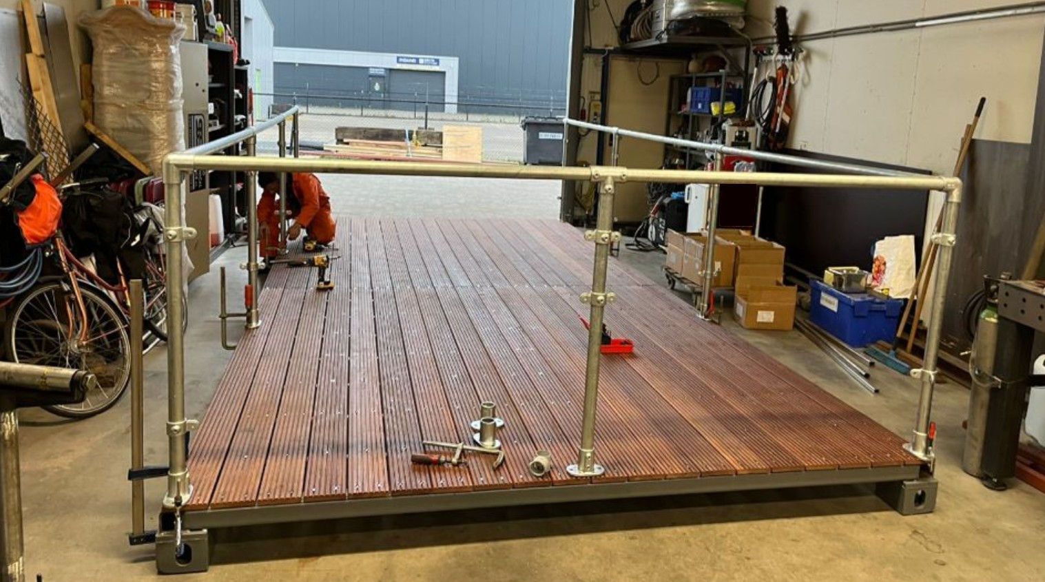 Koperen buizen in een metalen frame, mogelijk een warmteoverdrachtssysteem. Iemand werkt eraan in een werkplaats.