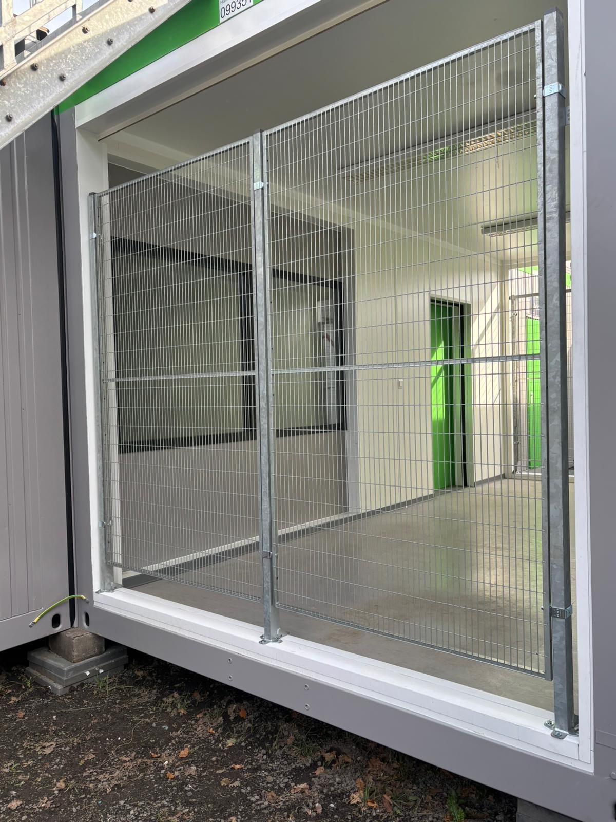 Metalen veiligheidshek voor een open deuropening van een grijs gebouw.