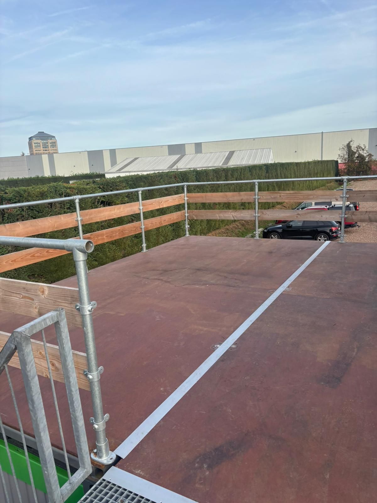 Perron met leuning, witte lijn, groene heg en een gebouw op een zonnige dag.
