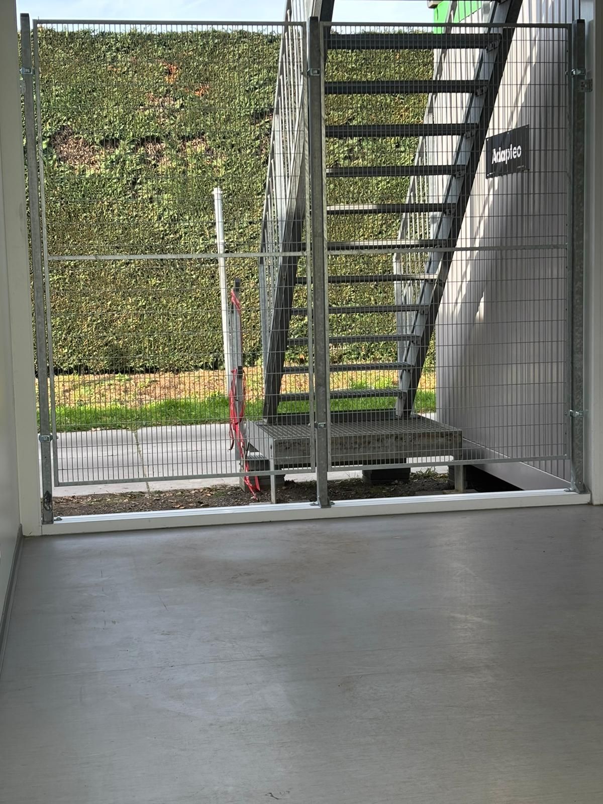 Een metalen trap achter een metalen hek, met een betonnen vloer op de voorgrond