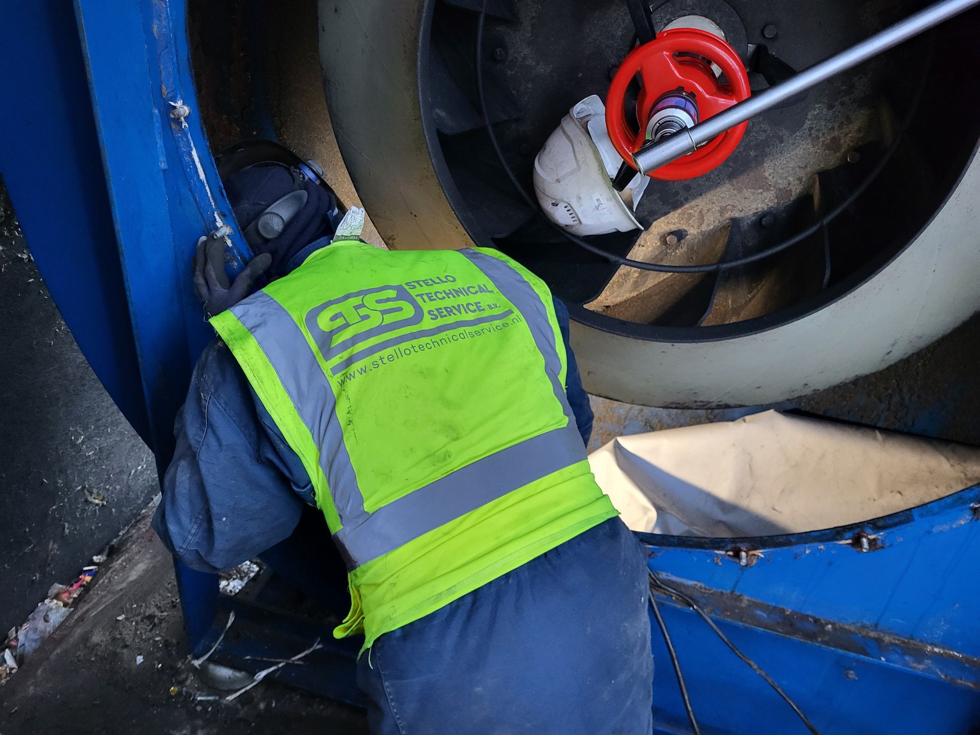 Een werknemer in een geel veiligheidsvest inspecteert machines met behulp van gereedschap.