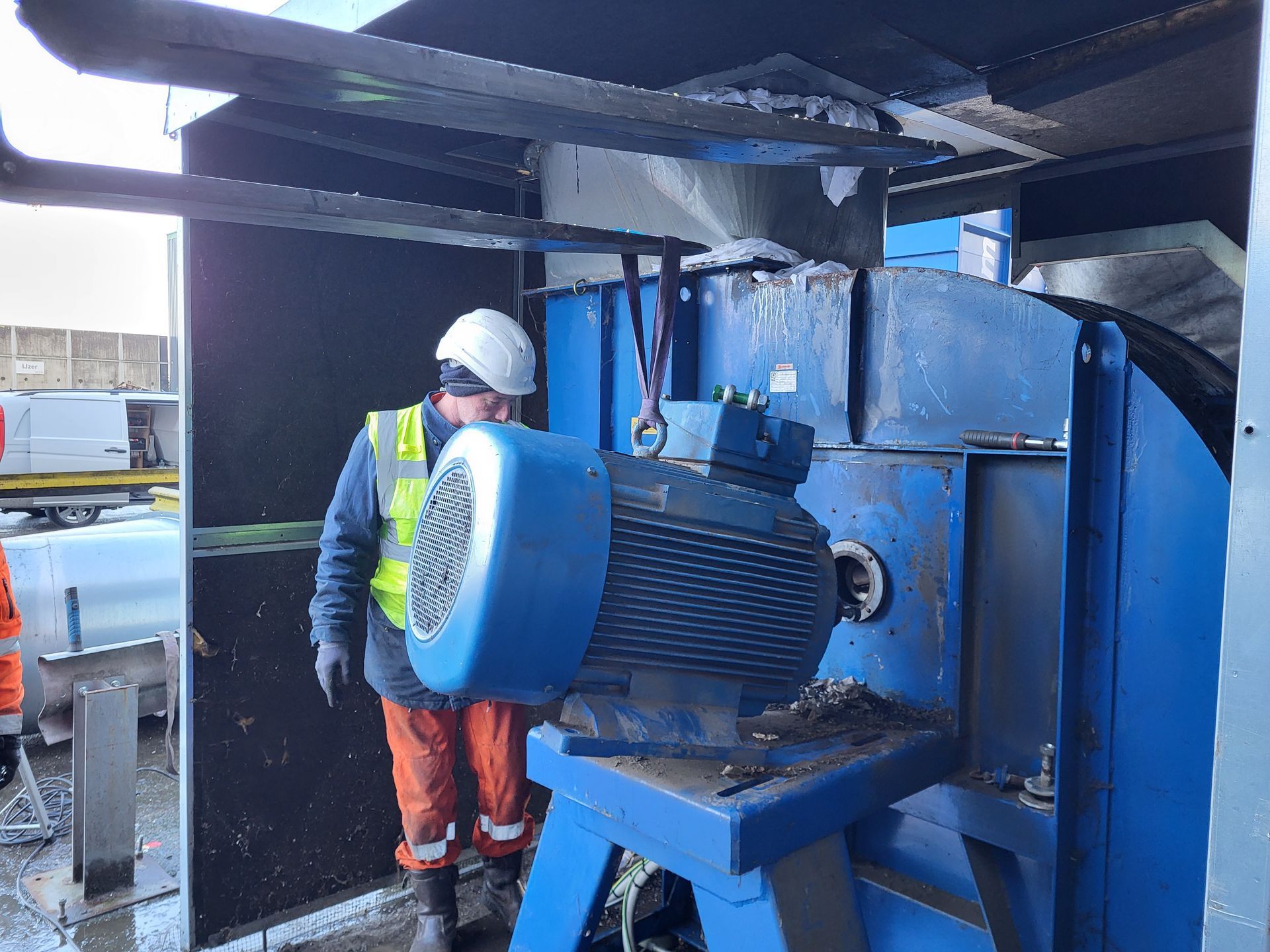Werknemer in veiligheidsuitrusting nabij een grote blauwe industriële machine.