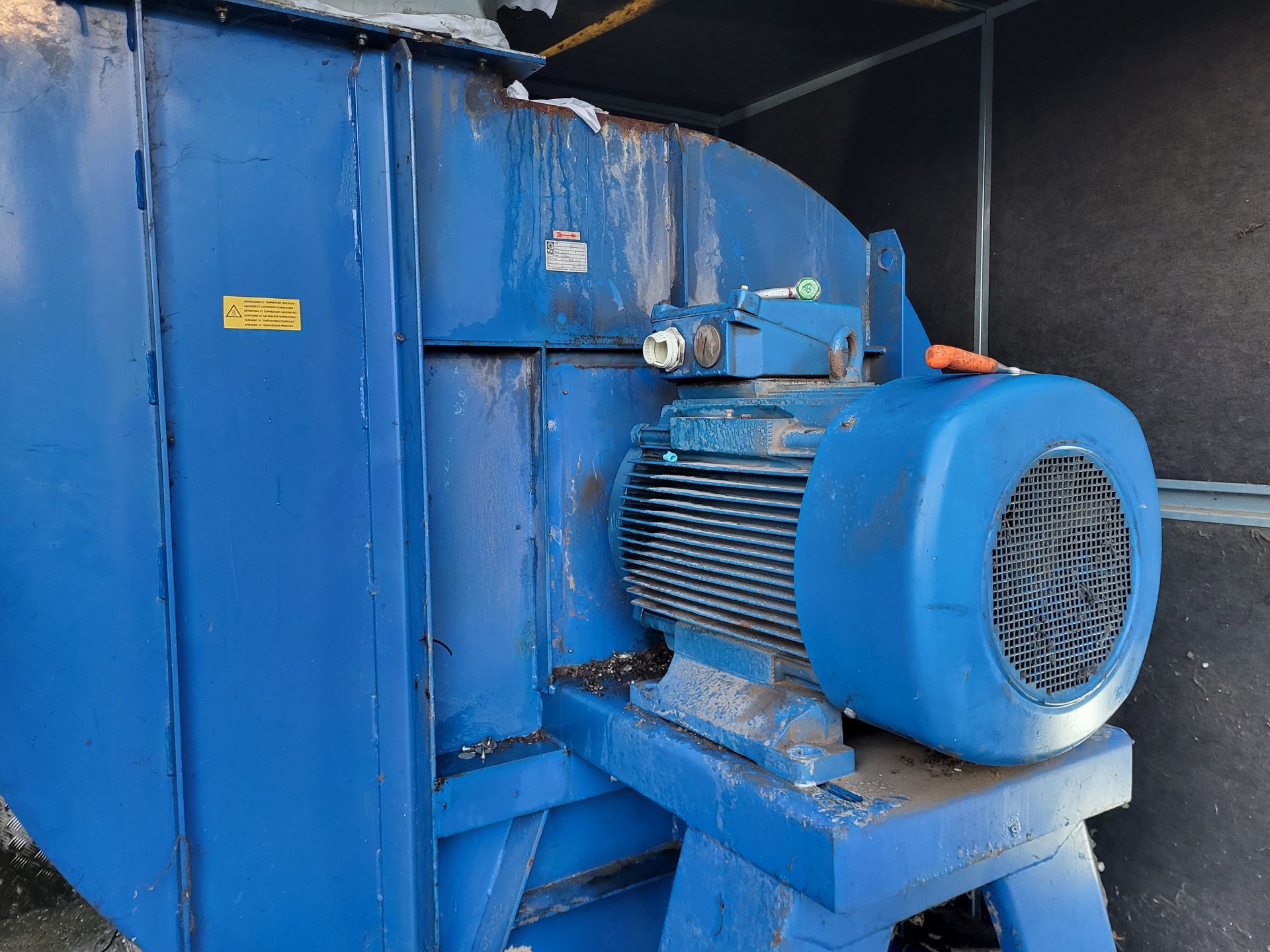 Blauwe industriële ventilator met motor, gemonteerd op een metalen voet, voor buitengebruik.