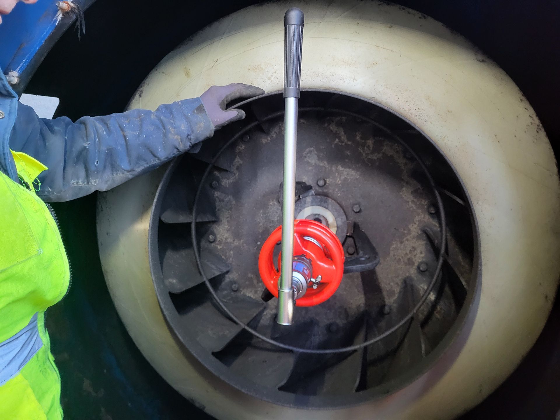Iemand die met een gereedschap een rood wiel in een groot, cirkelvormig mechanisme draait.