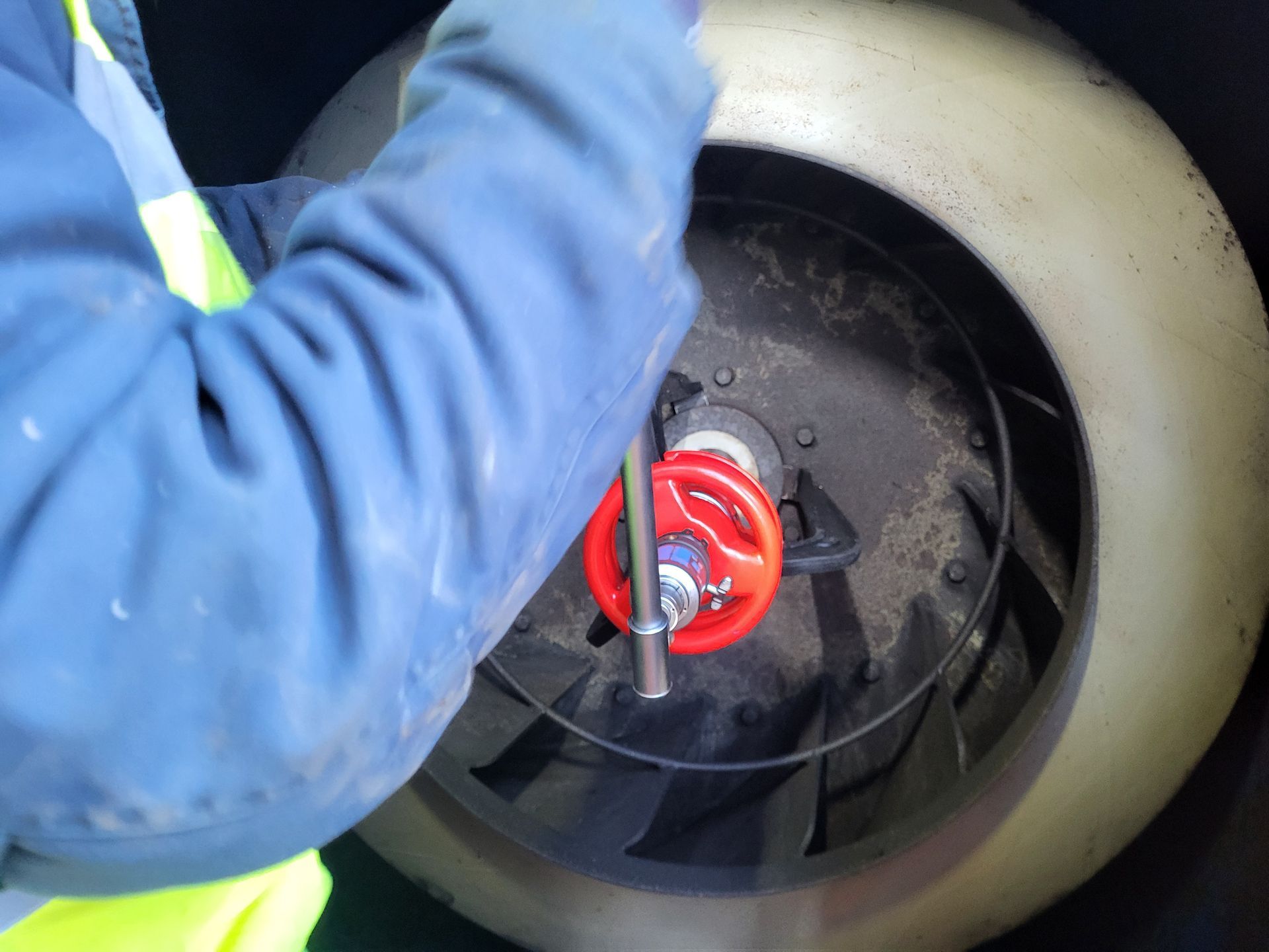 Persoon in blauwe overall die een ventilator met een rode klep onderhoudt.