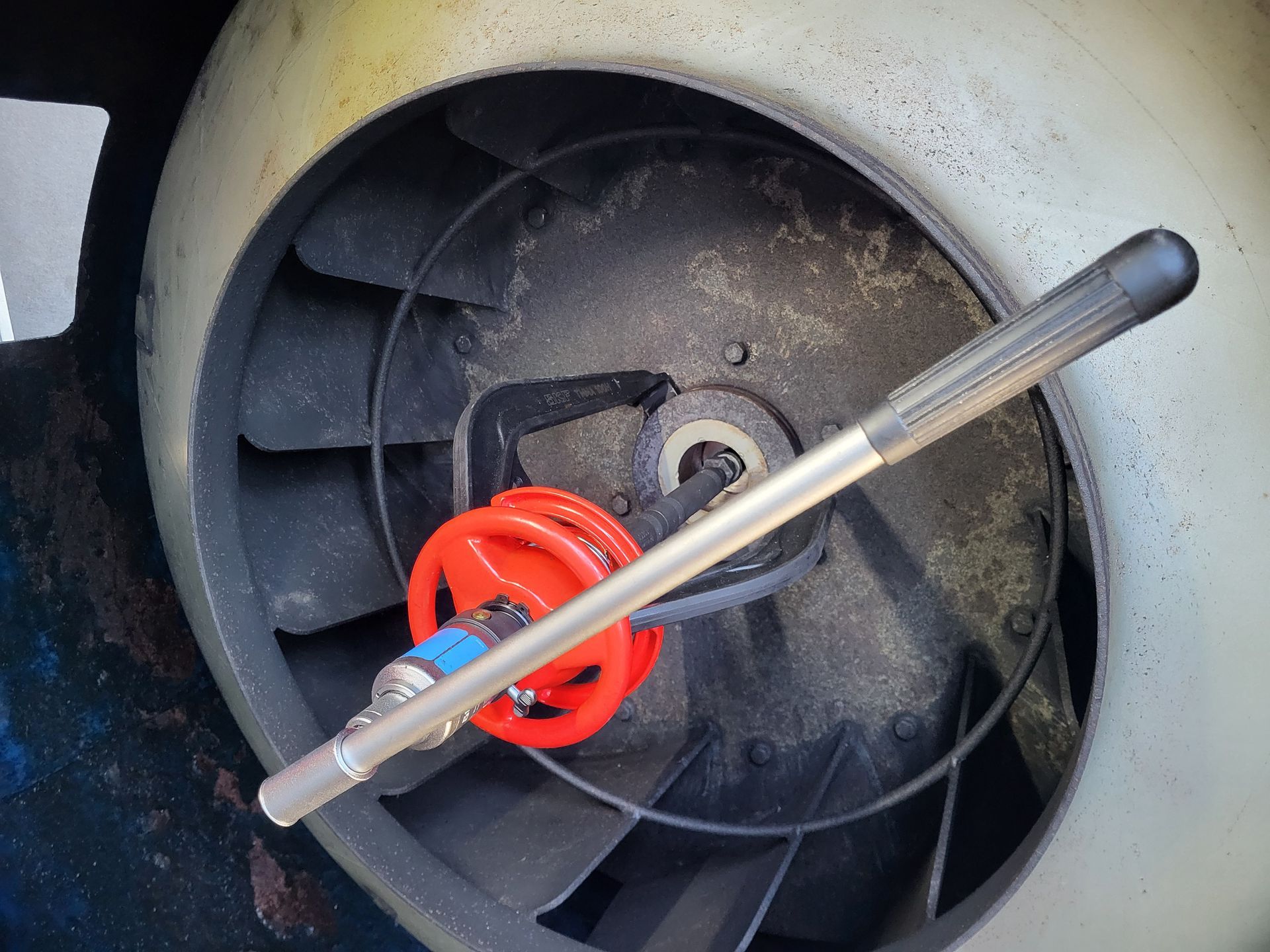 Een ventilator met een rood meetinstrument; de omgeving is industrieel en stoffig.