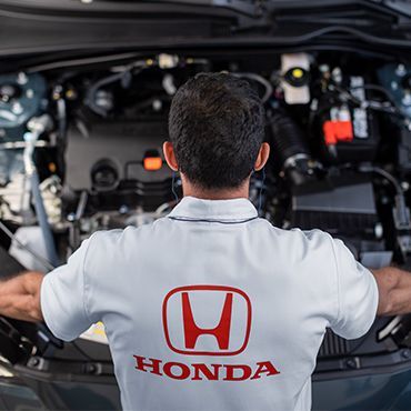 Mecânico de camisa branca da Honda, trabalhando no motor de um carro.