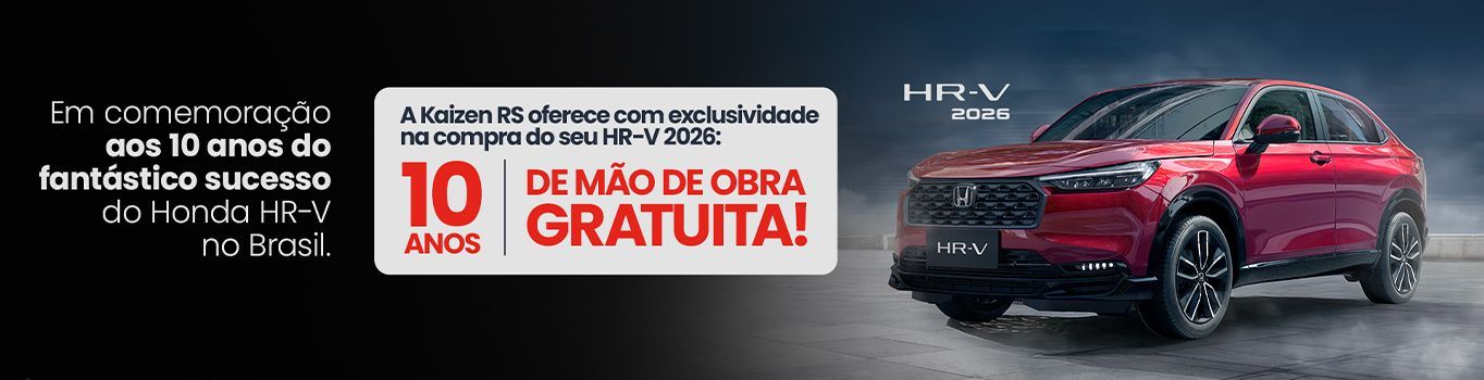 Um homem de blazer bege sorri enquanto usa um laptop em uma mesa com uma caneca de café e um carrinho de brinquedo.