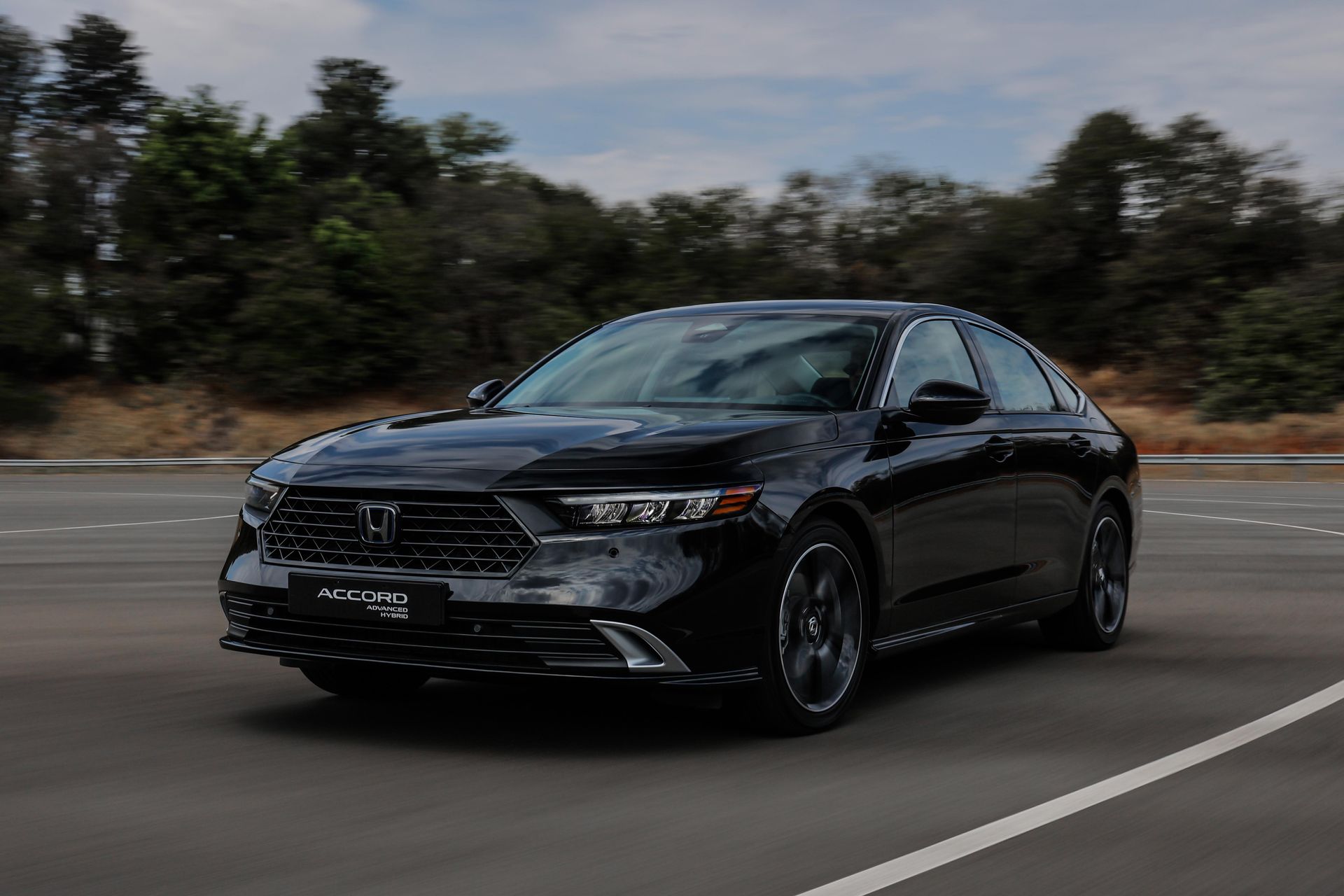 Sedan Honda preto dirigindo em uma estrada com árvores ao fundo.