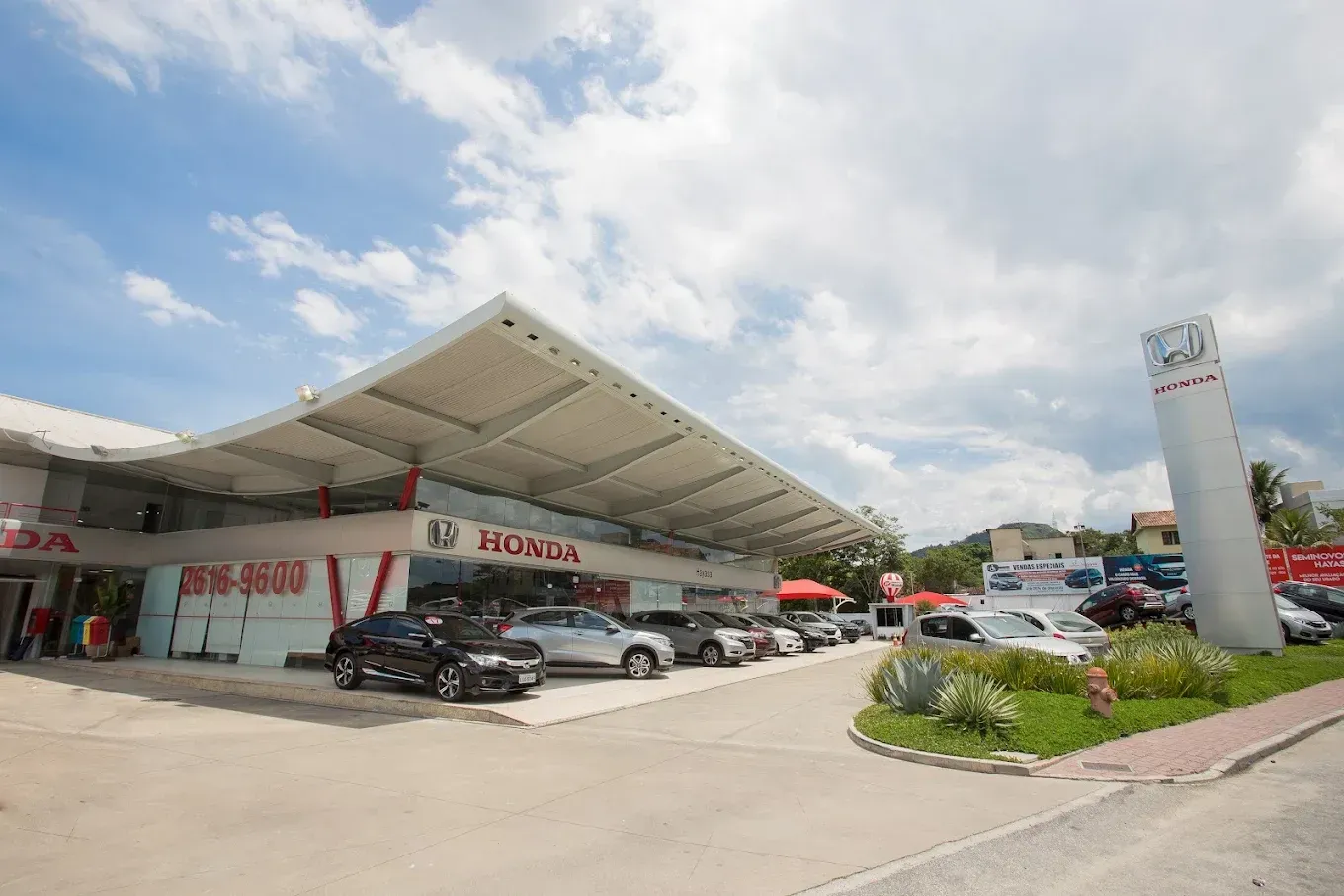 Concessionária Honda com bandeiras vermelhas; céu azul.