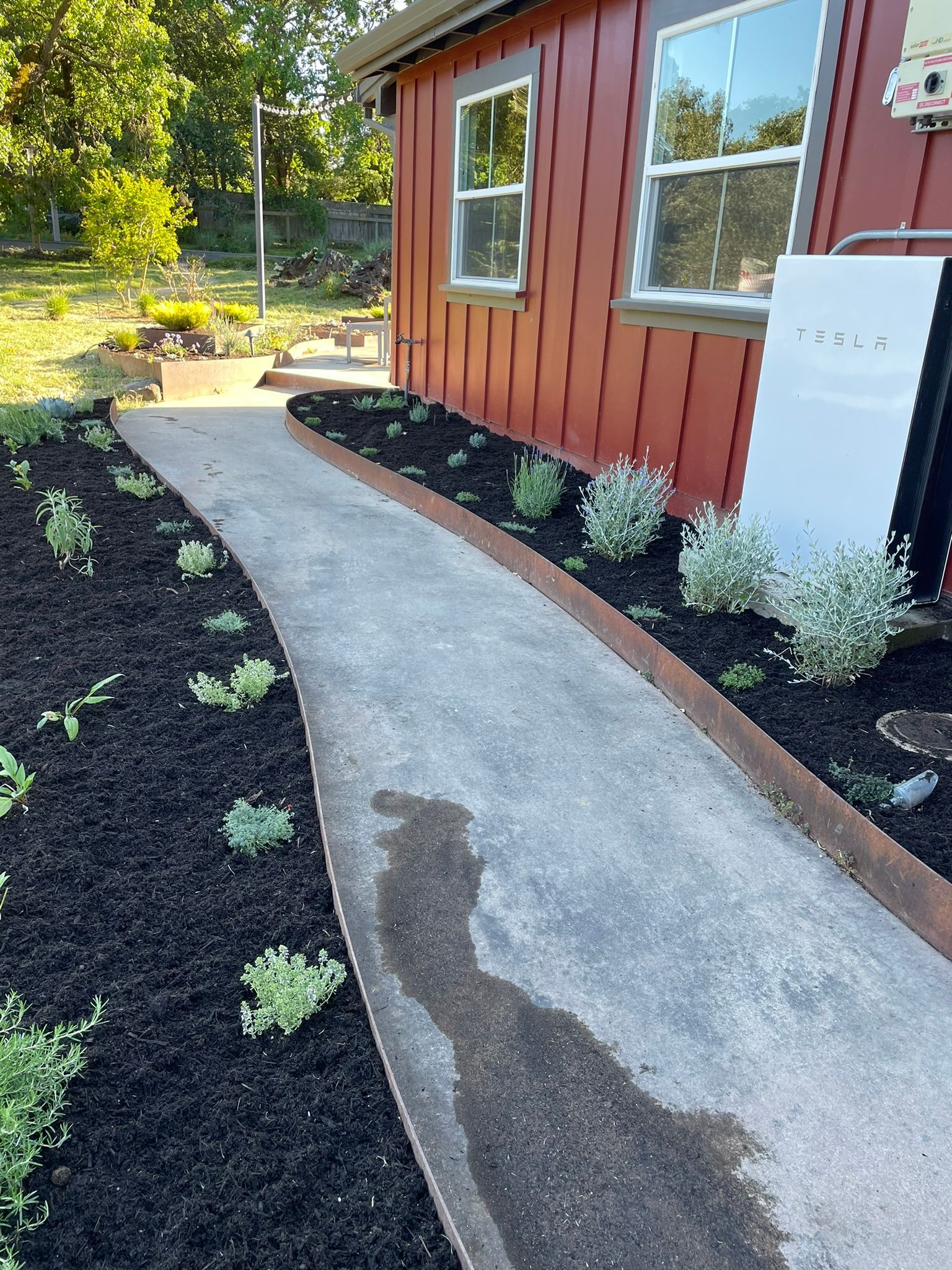 Curved concrete walkway beside a red house with black mulch and small green plants