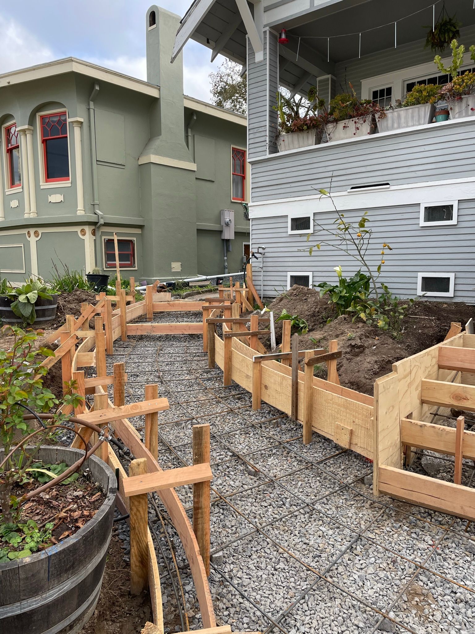 Raised garden beds along a gravel path beside houses and a porch