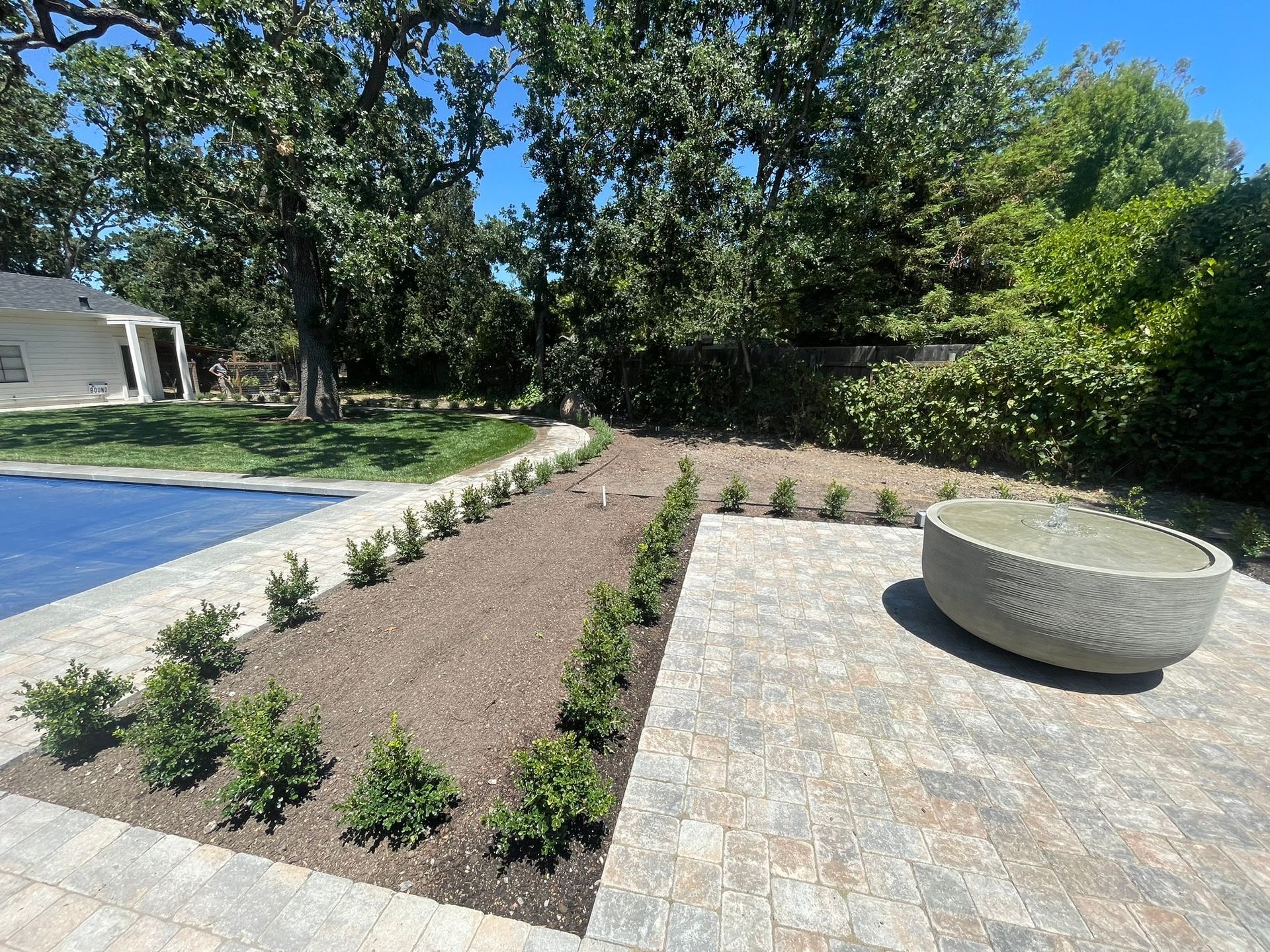 Landscaped backyard with gravel beds, small shrubs, a pool edge, and a round stone fire pit or planter.