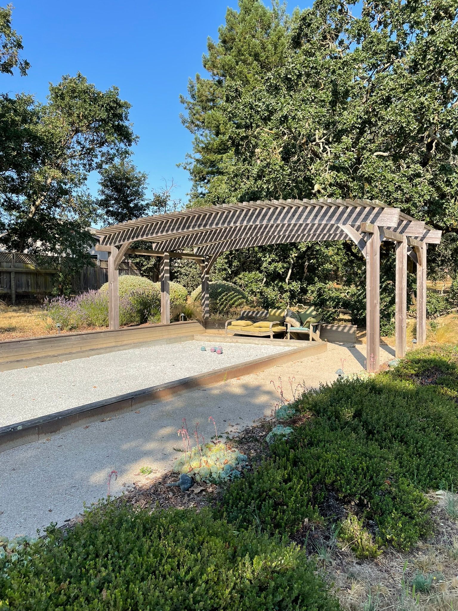 Wooden pergola beside a gravel path in a landscaped garden with trees and shrubs
