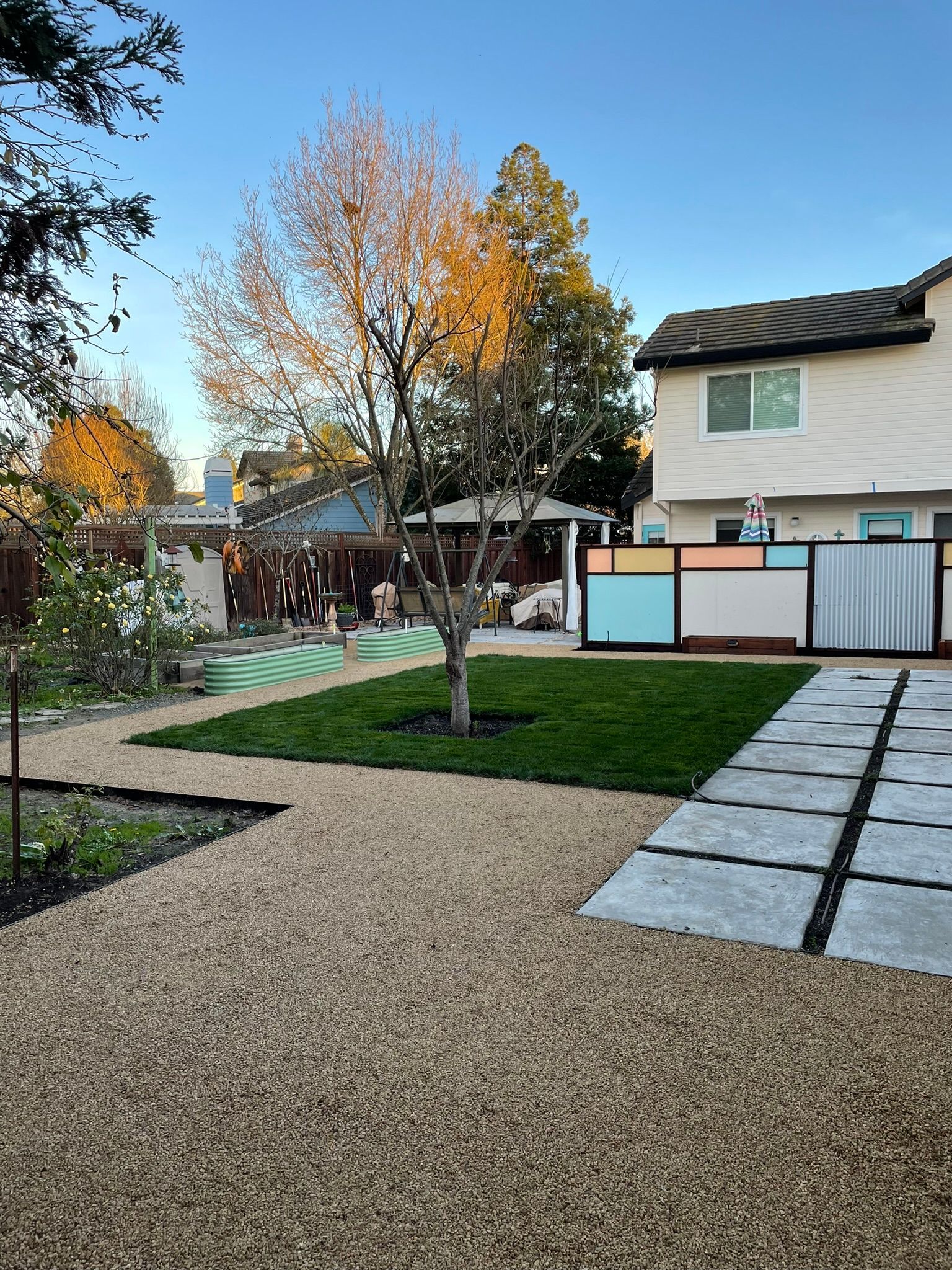 Backyard patio with gravel paths, stepping stones, grass, and a small tree beside a house