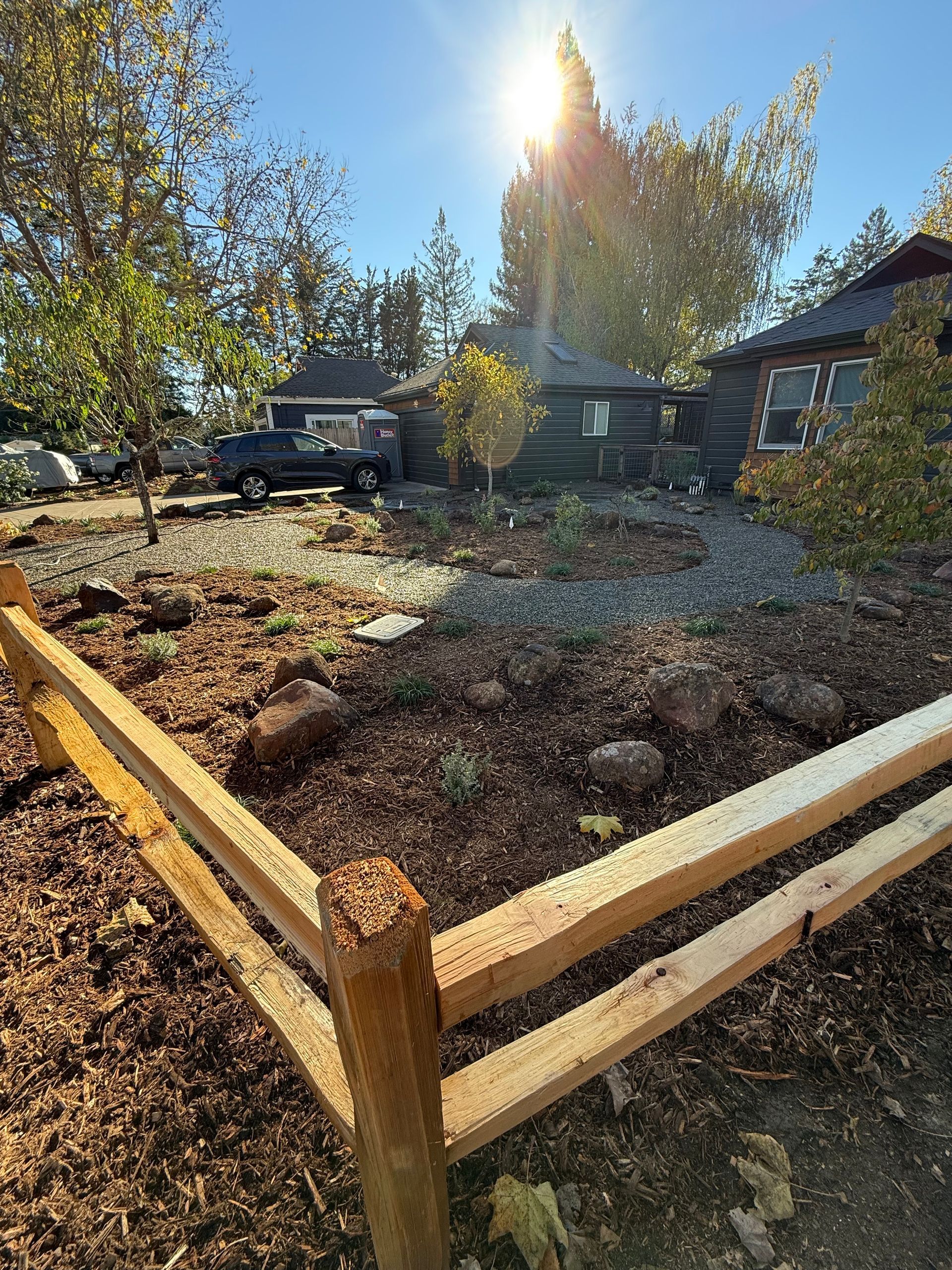 Wooden fence enclosing a garden bed beside a house, with trees and a truck in the background.