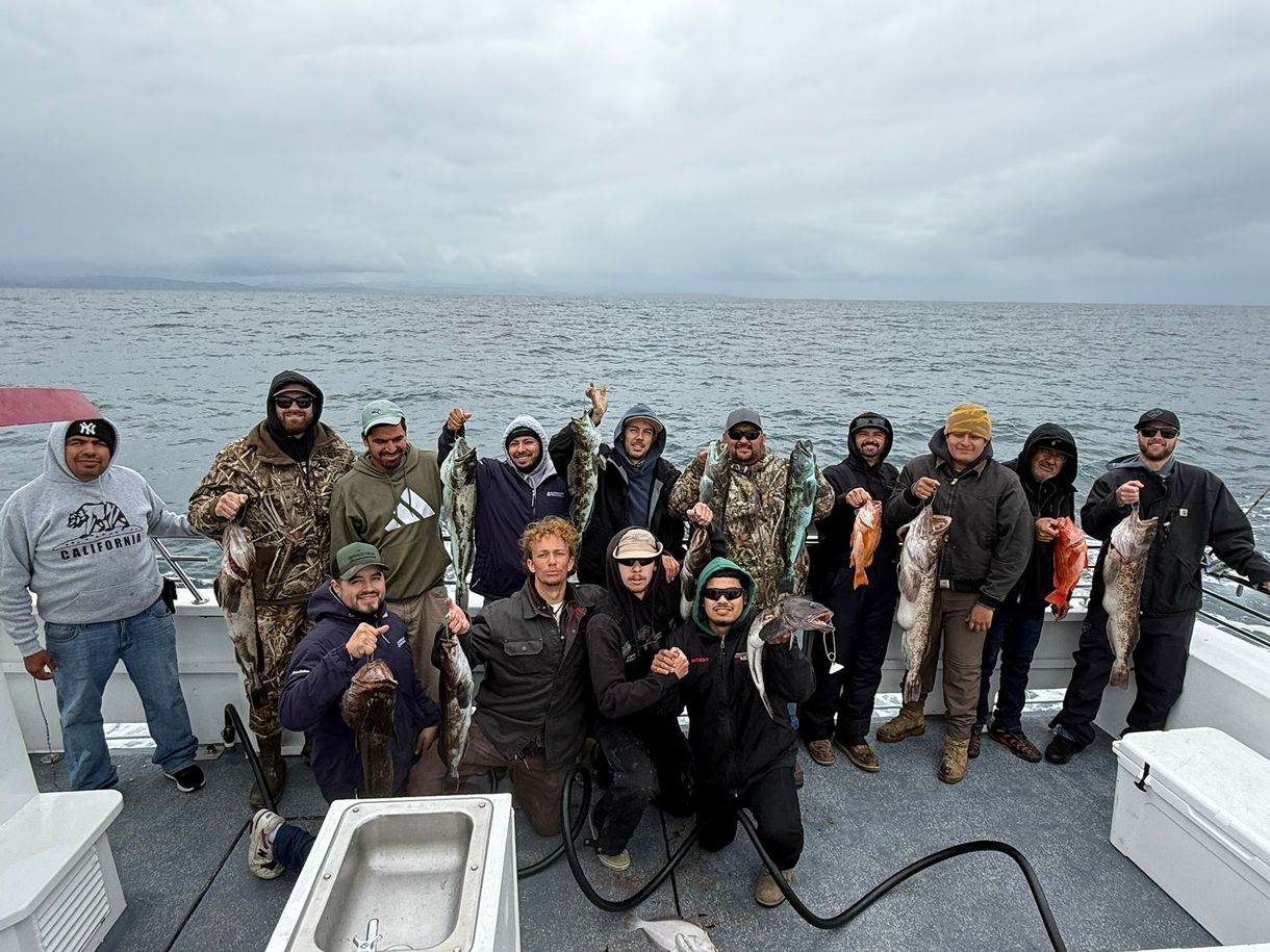 Group posing on a boat deck with a large fish on the left and open sea behind them