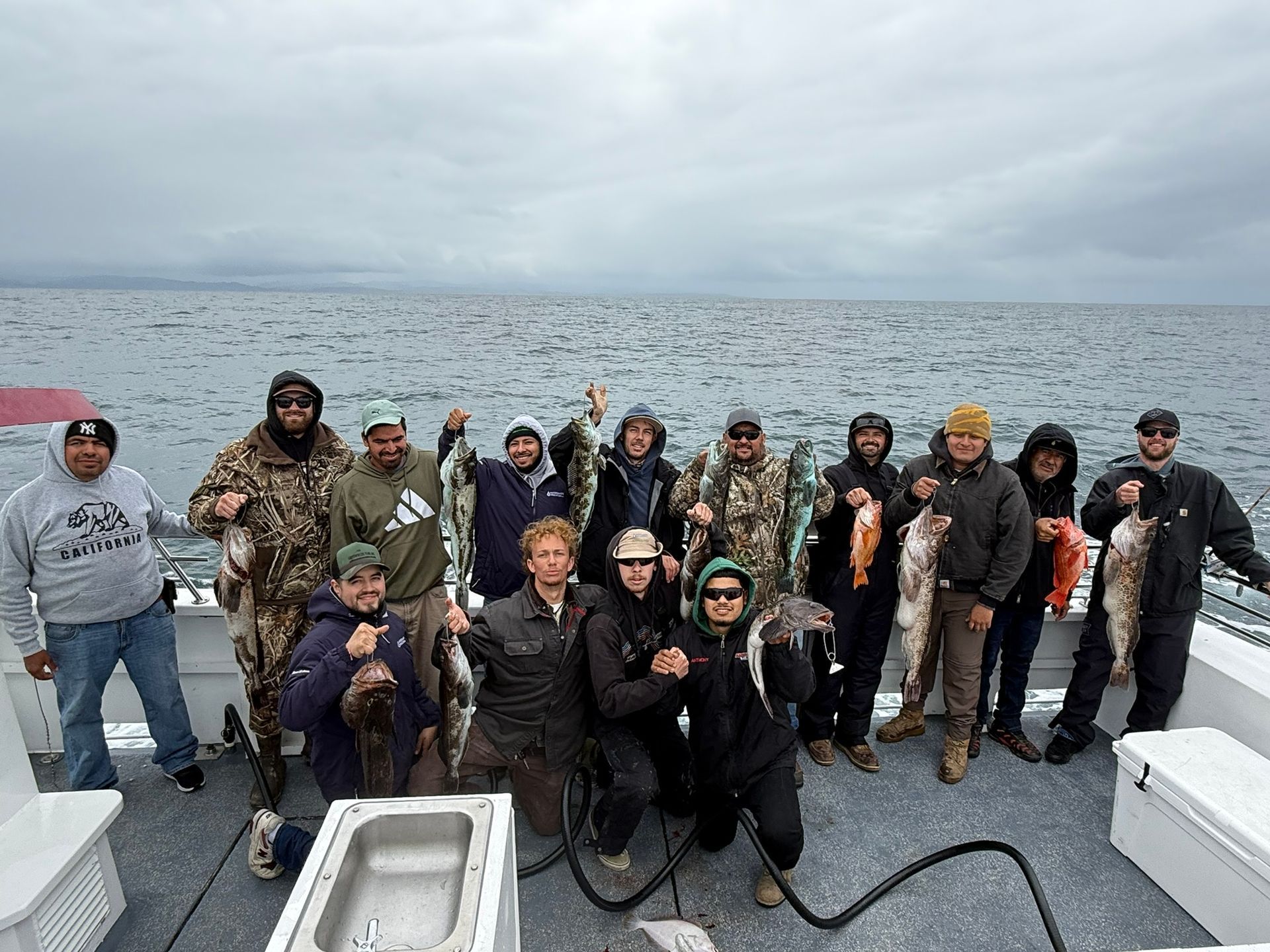 Group of people posing on a boat deck with ocean and cloudy sky behind them
