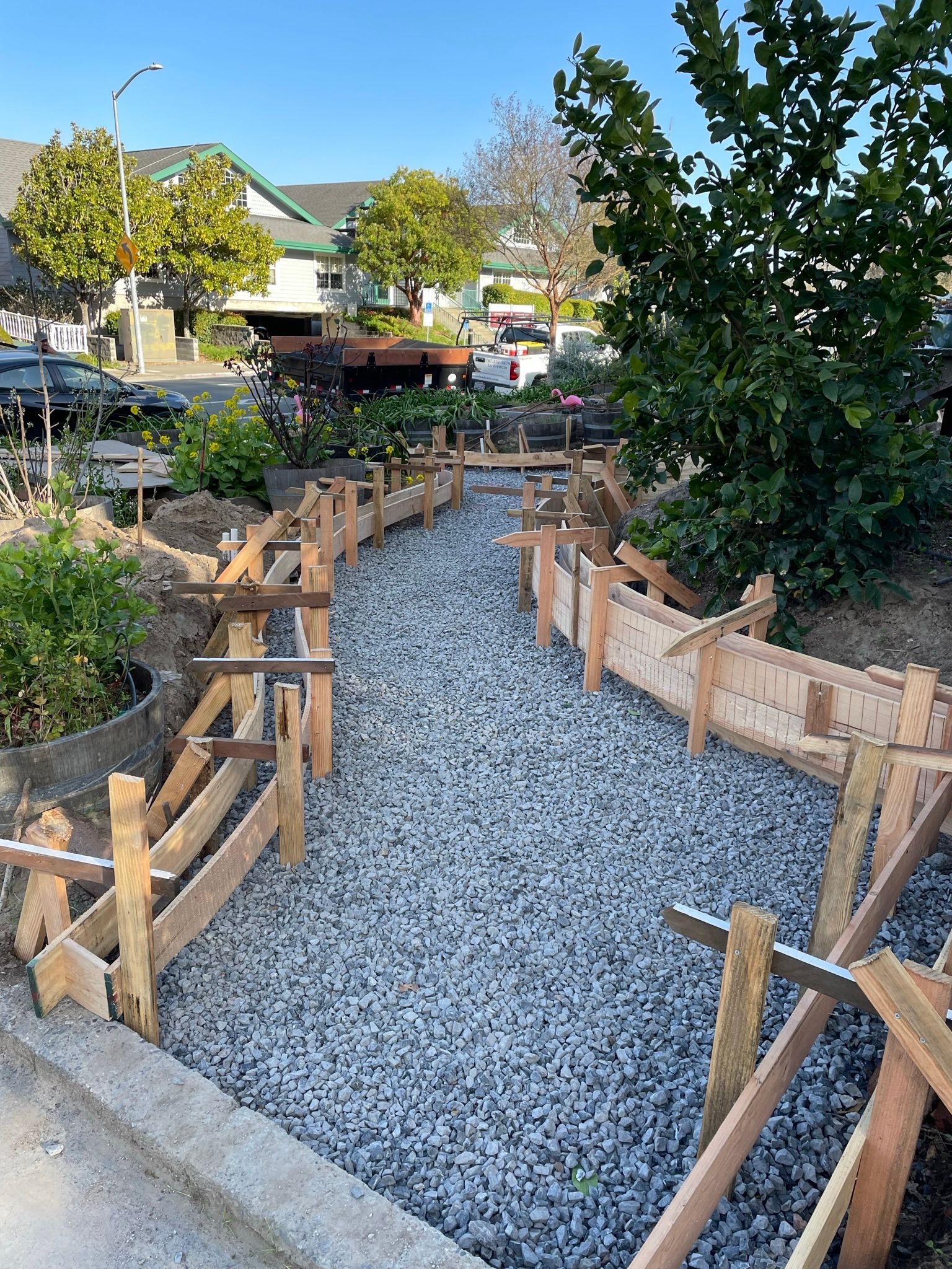 Gravel path with wooden railings winding through a landscaped garden near houses and trees
