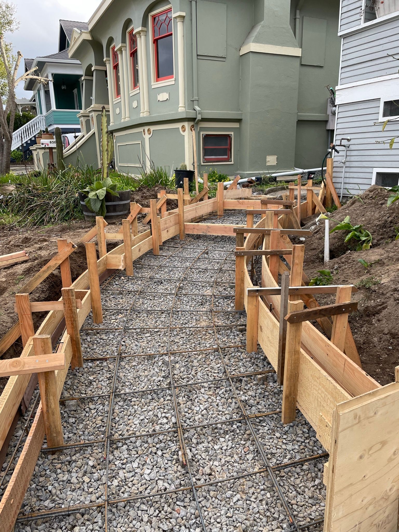 Wooden concrete forms lining a gravel pathway beside a gray house under construction