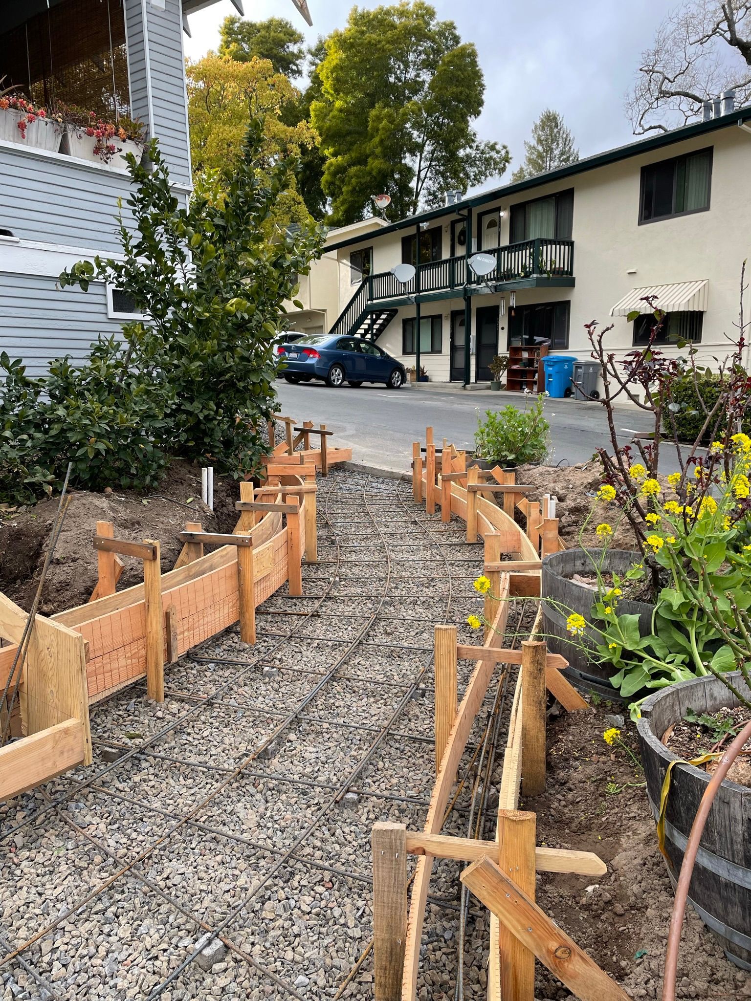 Gravel path lined with wooden borders leads to apartment buildings and trees in a courtyard.