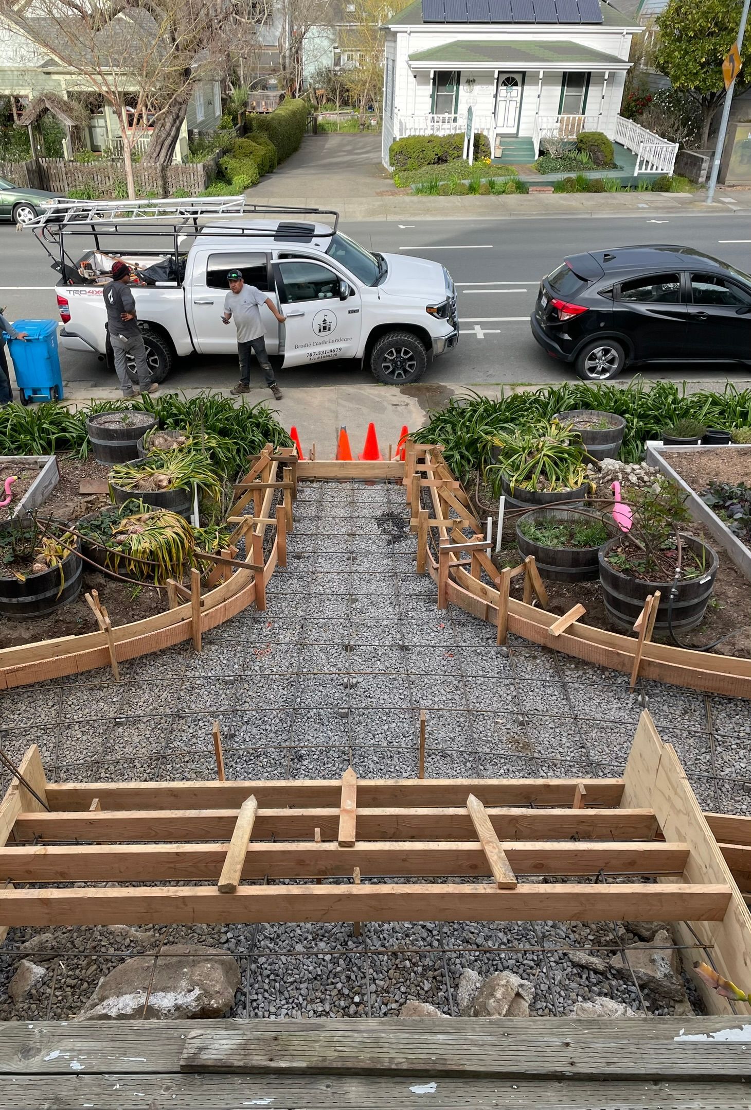 Front yard renovation with stone walkway, raised garden beds, and parked white truck and black SUV on the street
