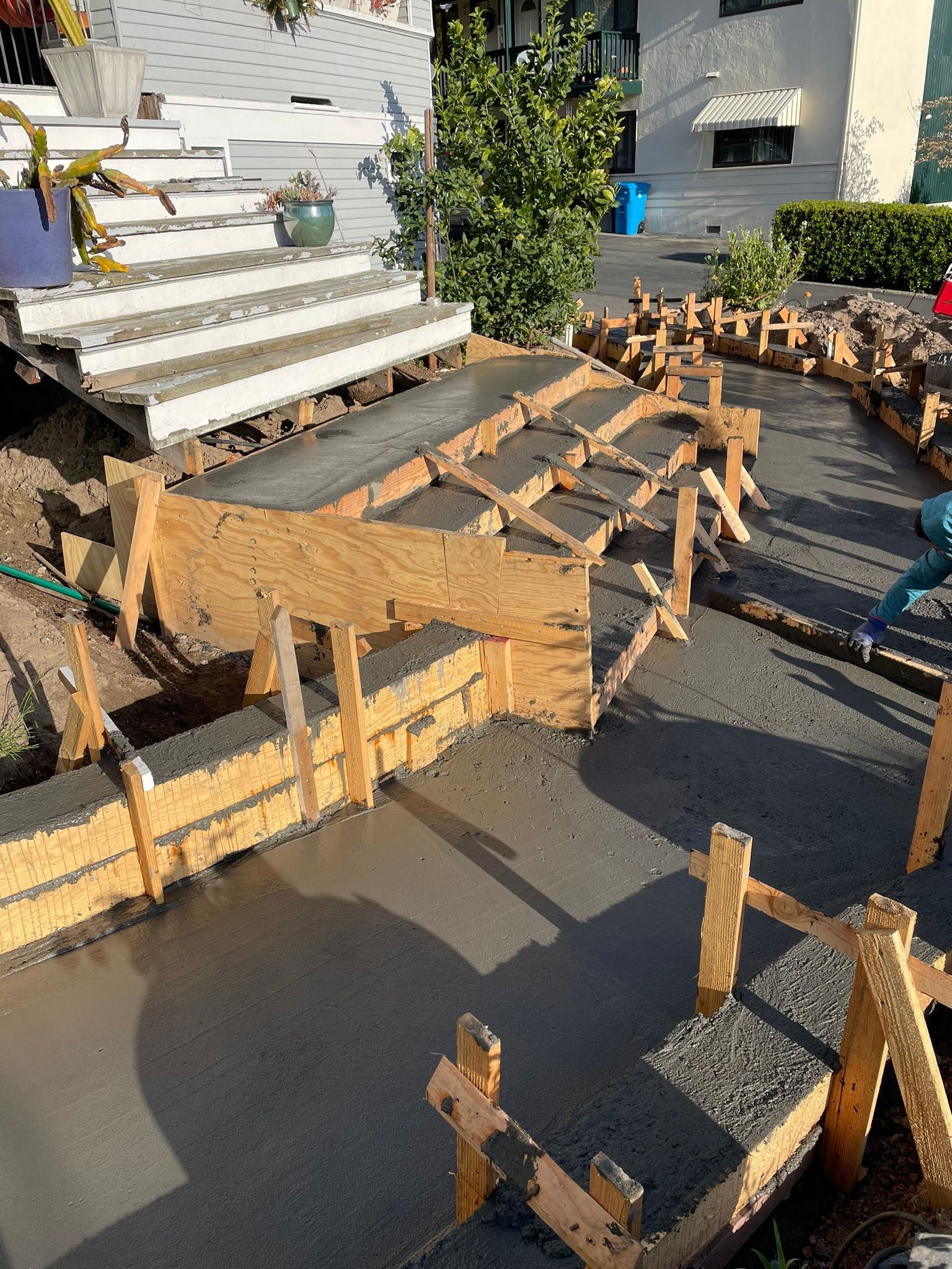 Wooden formwork laid for a curved concrete walkway beside a white house and steps